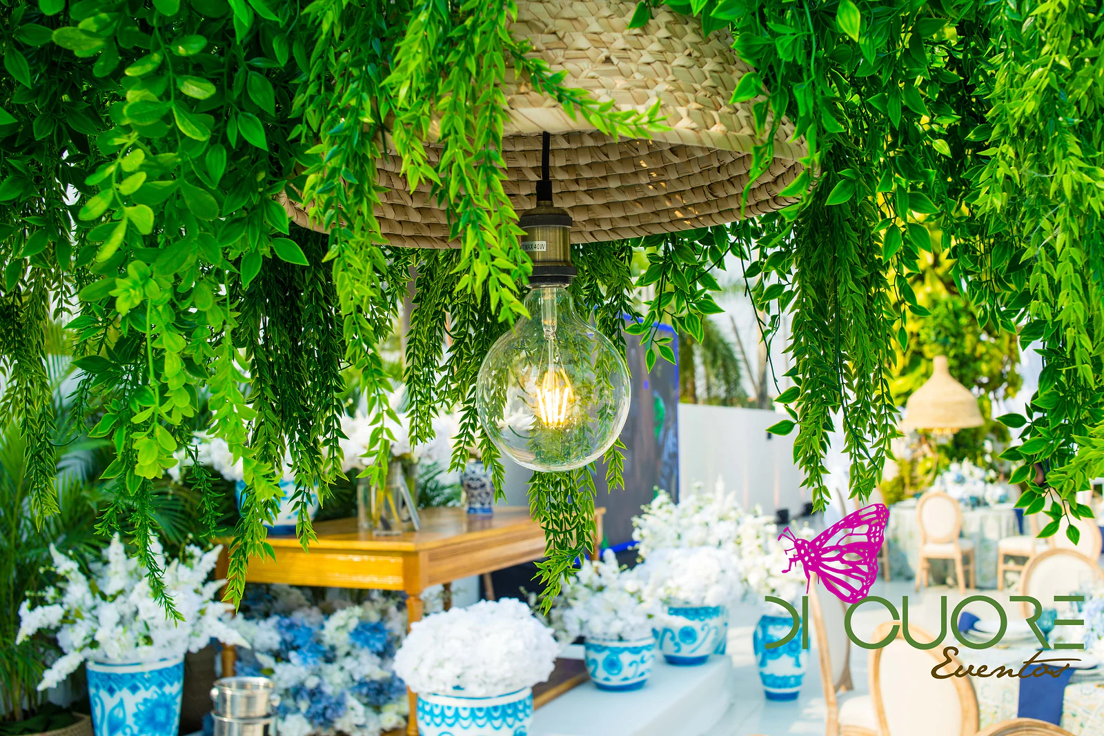 Straw pendant lamp with a globe bulb among cascades of foliage, above a timber sideboard with blue-and-white vases full of white flowers