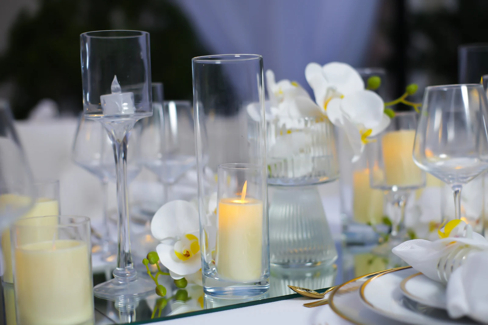 Velas em copos de vidro, taças e orquídeas brancas sobre um friso de espelho