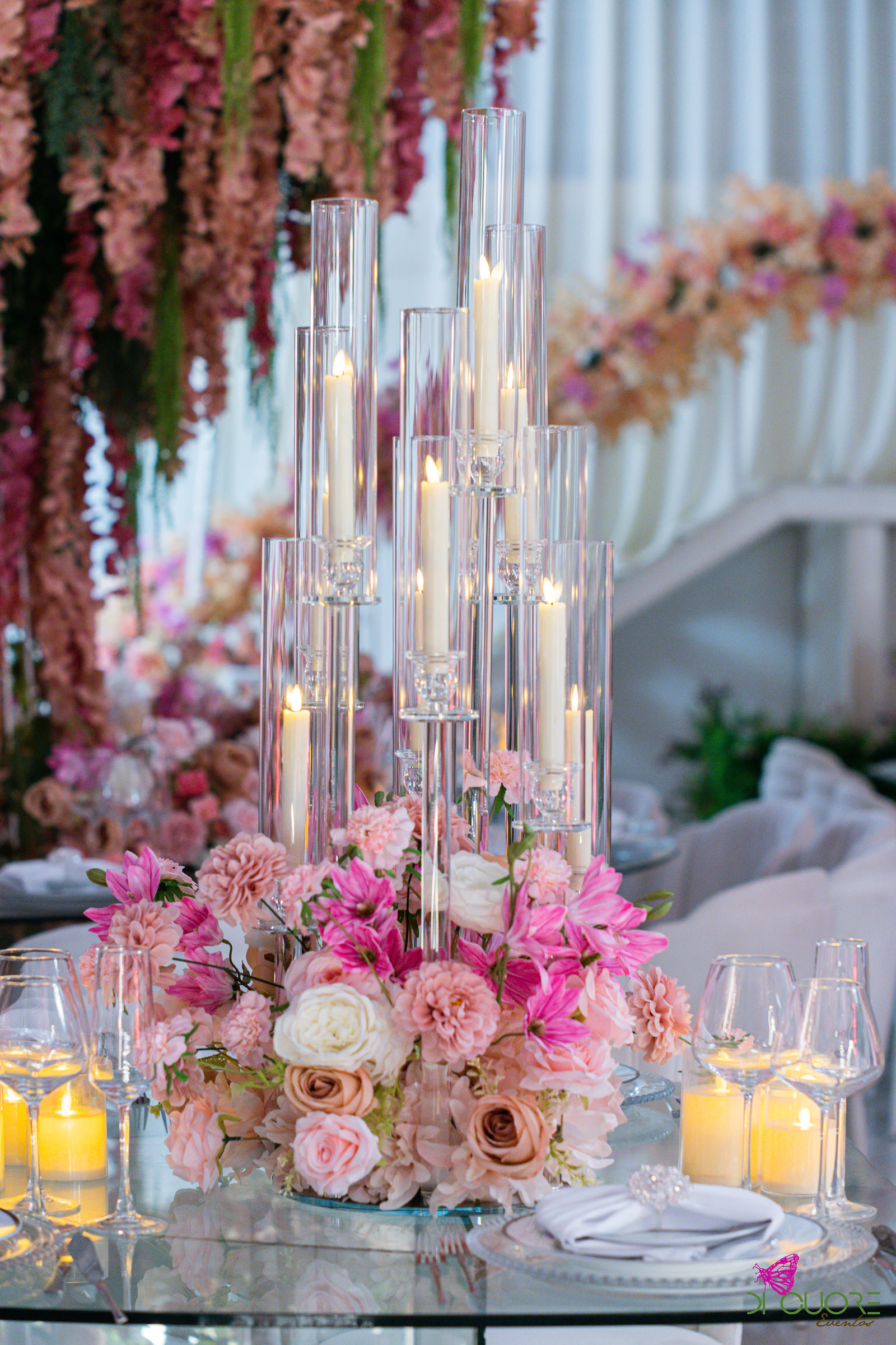 Candelabro de vidro com velas altas e flores cor-de-rosa, sob flores suspensas em coral e rosa