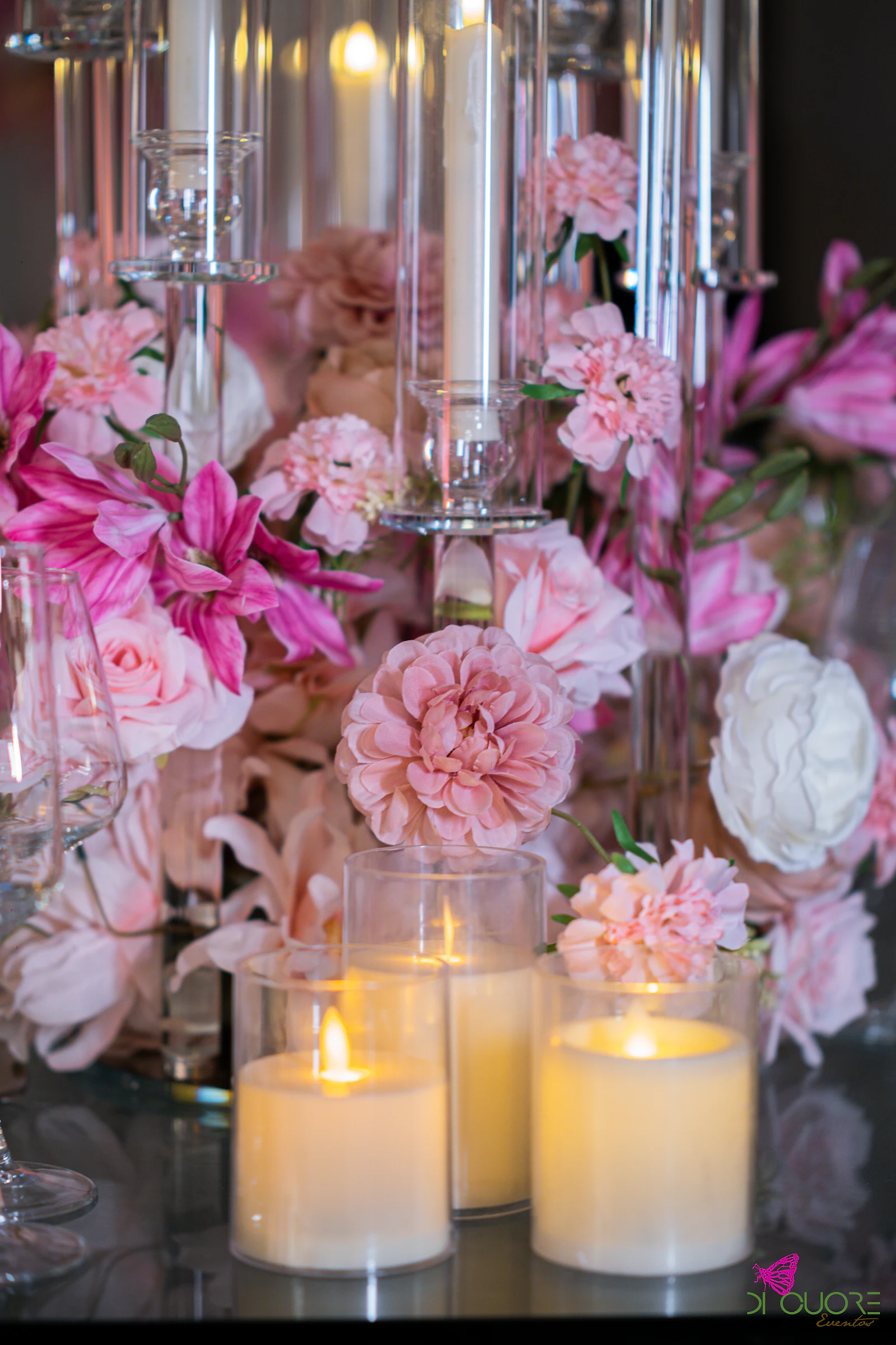 Rosas e flores cor-de-rosa entre velas e candelabros de vidro, sobre uma mesa de vidro