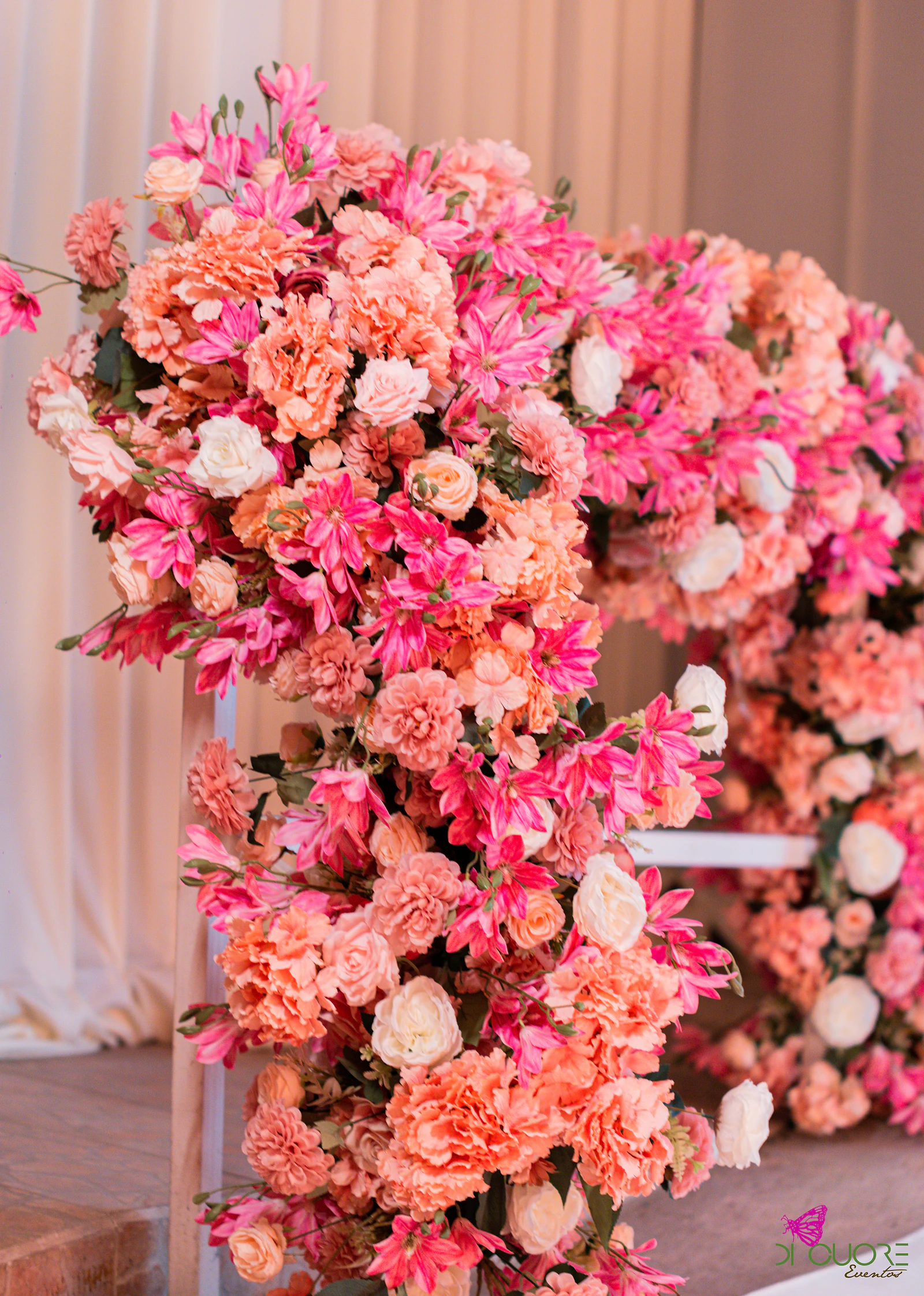 Maciço de flores cor-de-rosa, coral e cremes numa estrutura em arco