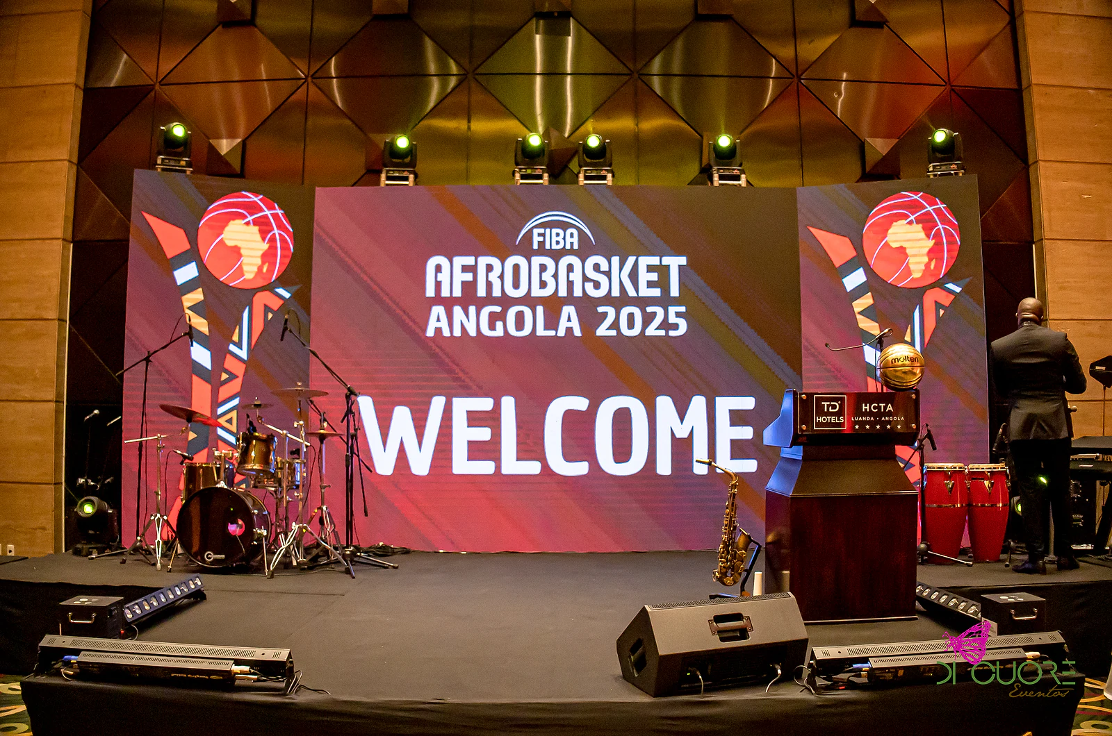 Palco com o ecrã “Welcome” do FIBA AfroBasket Angola 2025, bateria, saxofone e atril