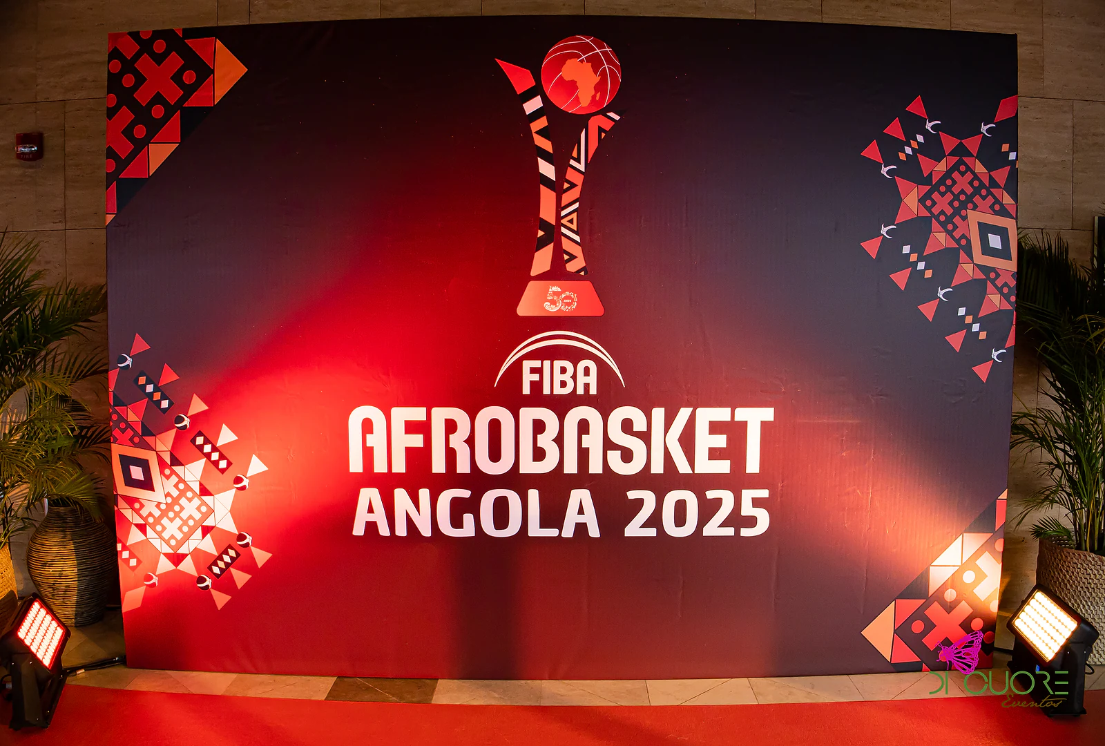 Painel preto e vermelho com o logótipo do FIBA AfroBasket Angola 2025 e padrões geométricos, iluminado por projectores