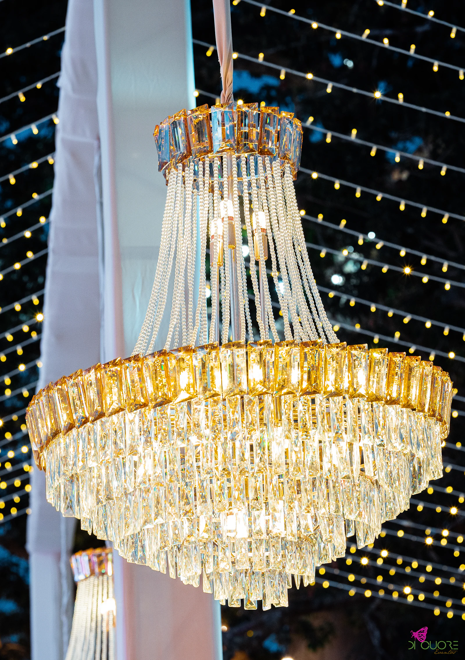 Lustre de cristal dourado aceso, em primeiro plano, entre cortinas de luzes à noite