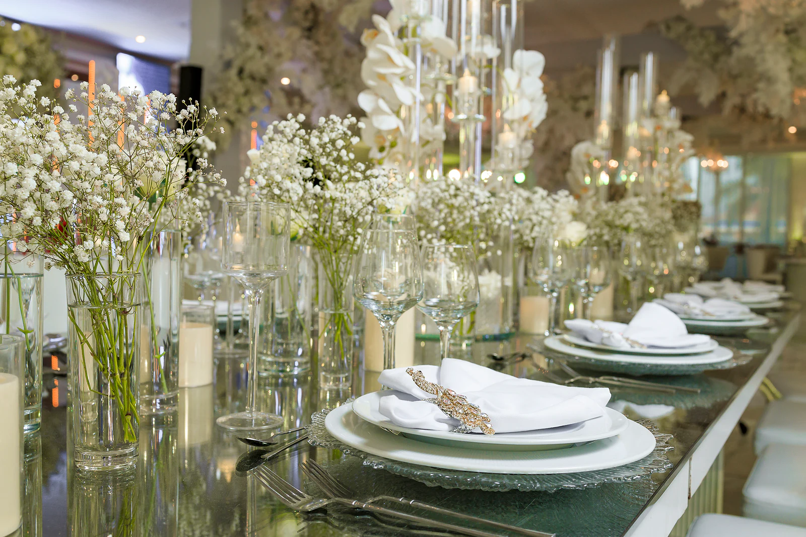 Mesa comprida de espelho com jarras de gipsófila, orquídeas brancas e velas ao longo dos lugares postos