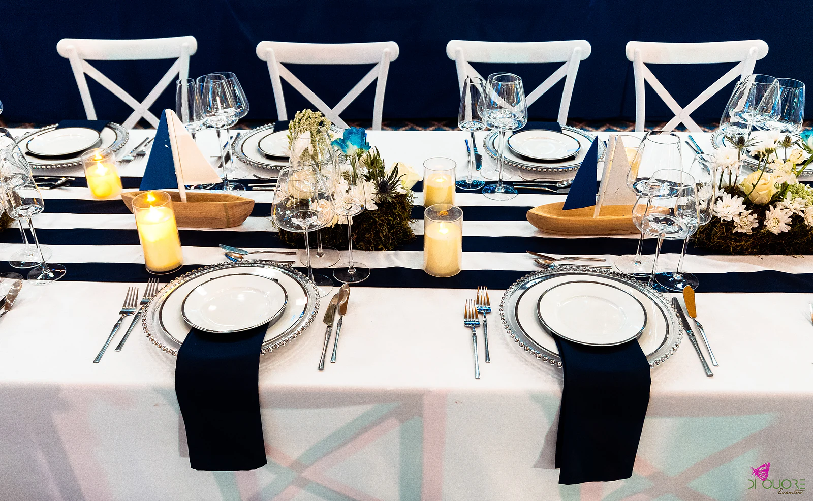 Place settings with silver-rimmed plates, navy napkins, candles and small wooden boats on the striped runner