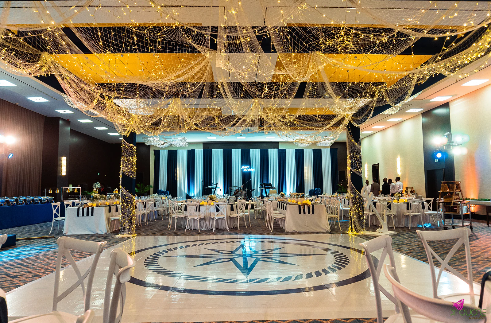 White dance floor with a navy compass rose beneath a canopy of fishing net strung with lights