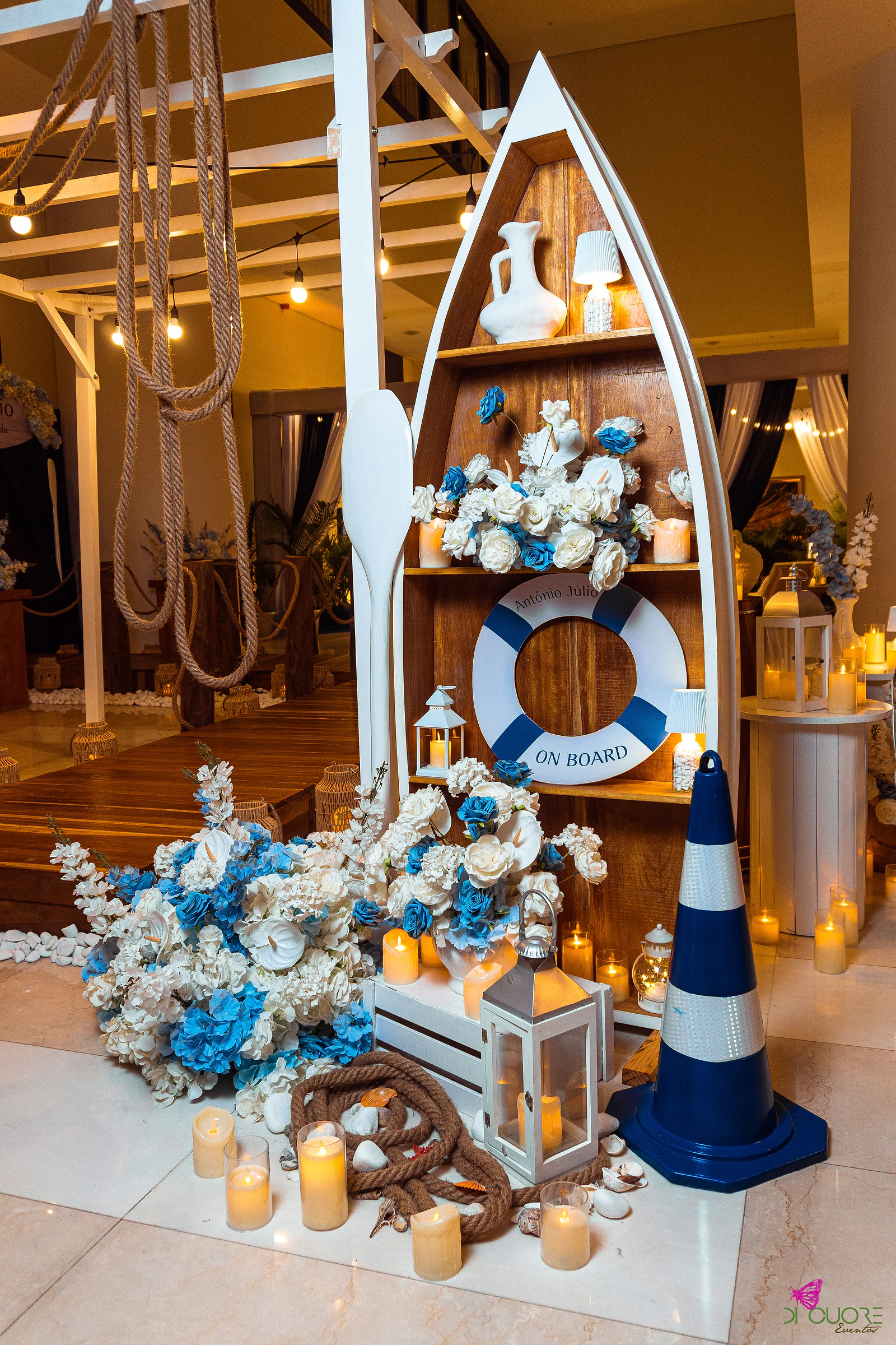 Boat-shaped shelf with an On Board lifebuoy, jugs, candles and blue and white flowers, beside a blue and white cone