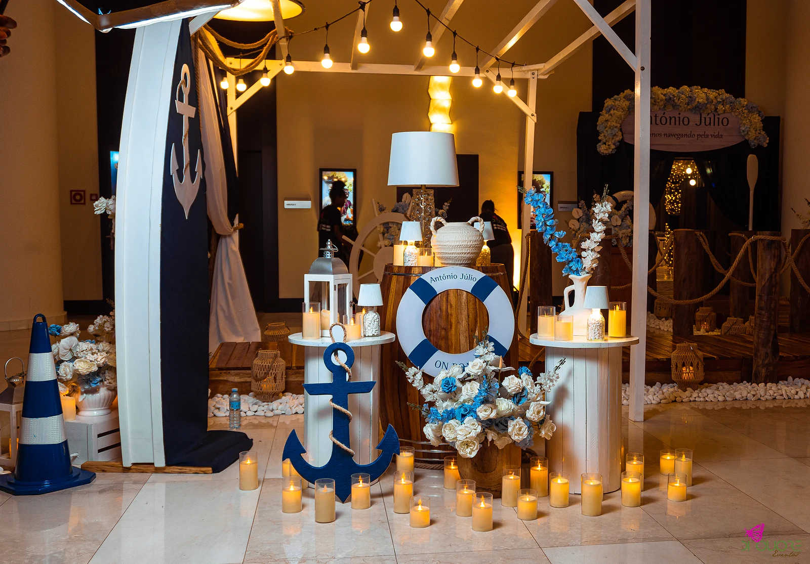 Entrance corner with a blue anchor on a white pedestal, a lifebuoy bearing the name António Júlio on a barrel, lanterns, lamps and many candles on the floor