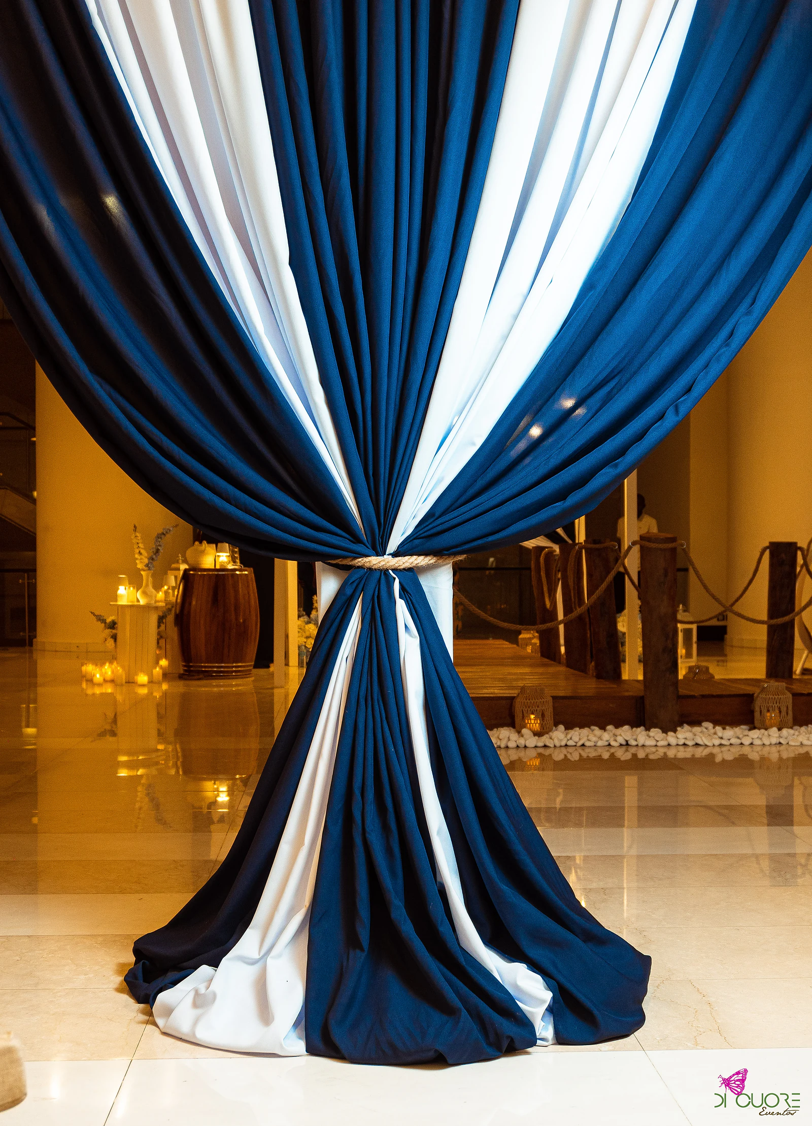 Navy and white striped drape tied with a rope, with the wooden jetty, ropes and white pebbles beyond