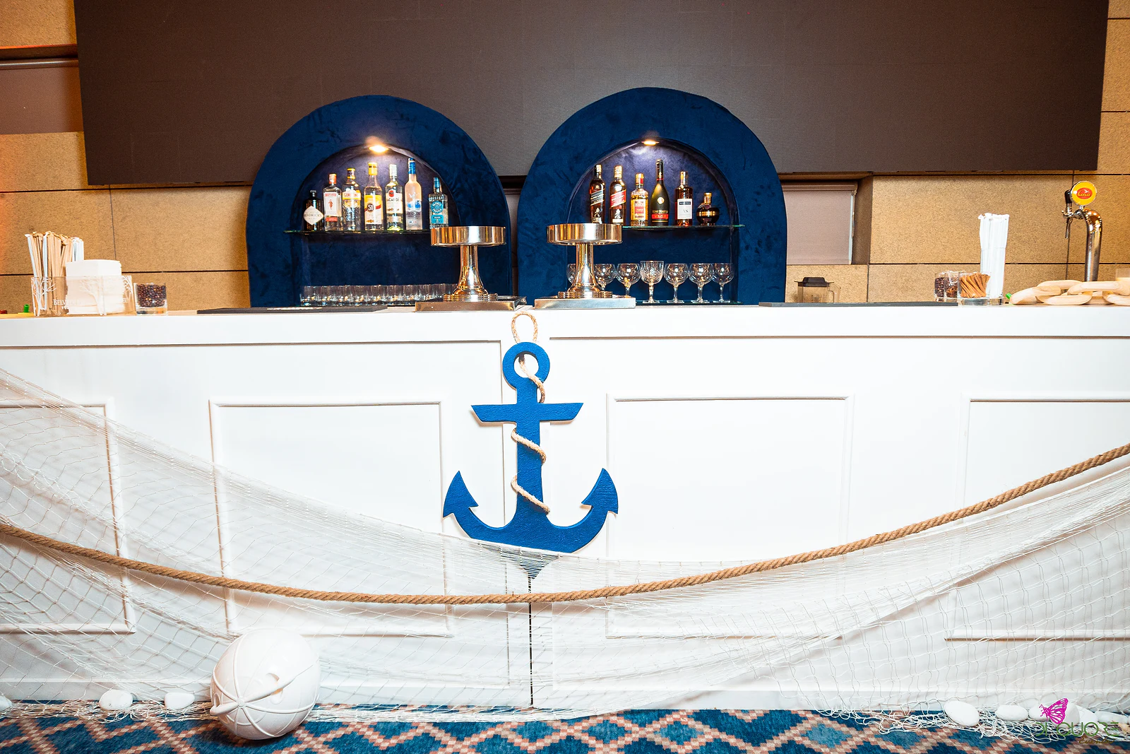 White bar with two navy arched shelves, a large blue anchor, fishing net and thick rope strung across the front