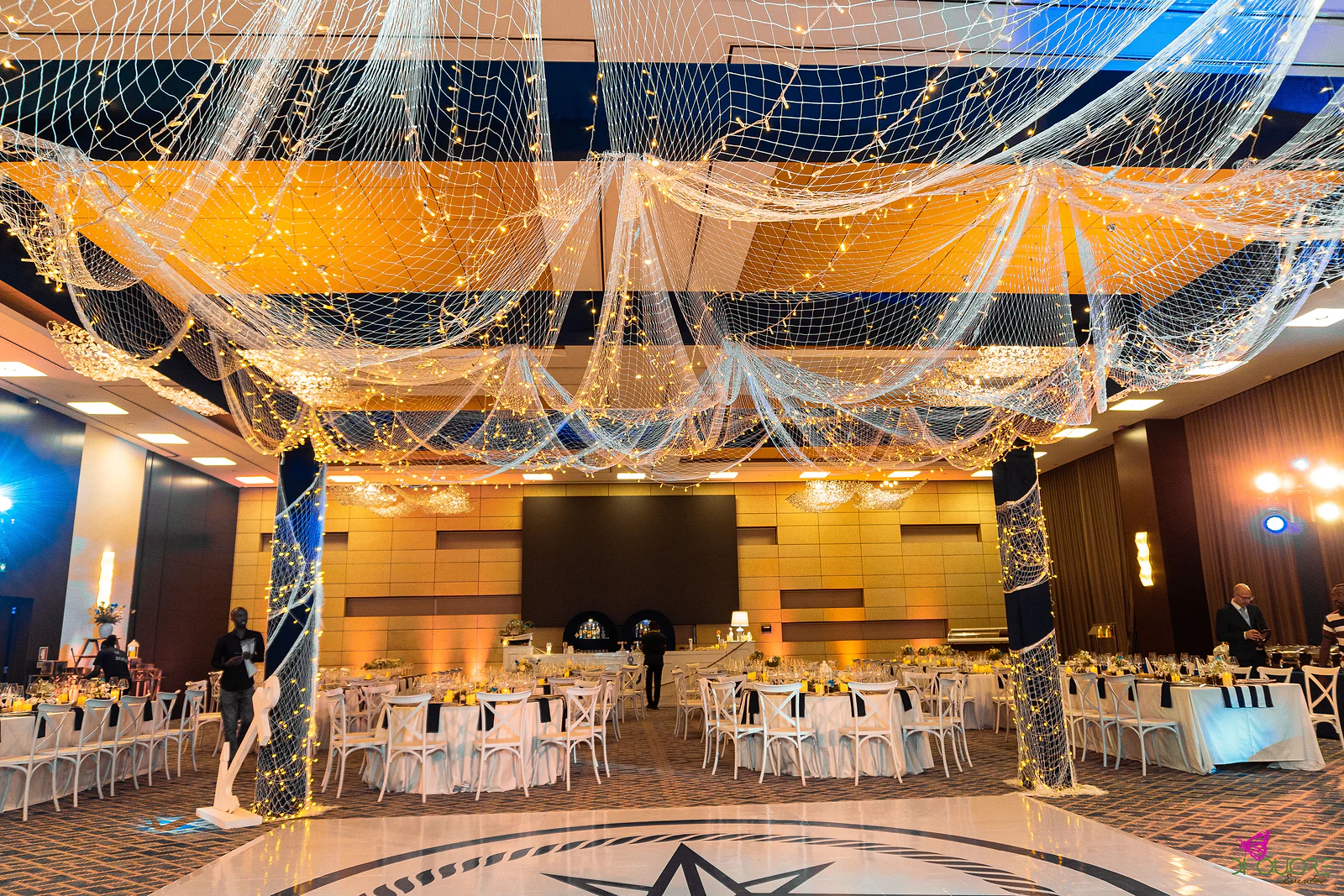 Ceiling covered in netting with fairy lights, between net-wrapped columns, above the dance floor with its compass rose and laid tables around it