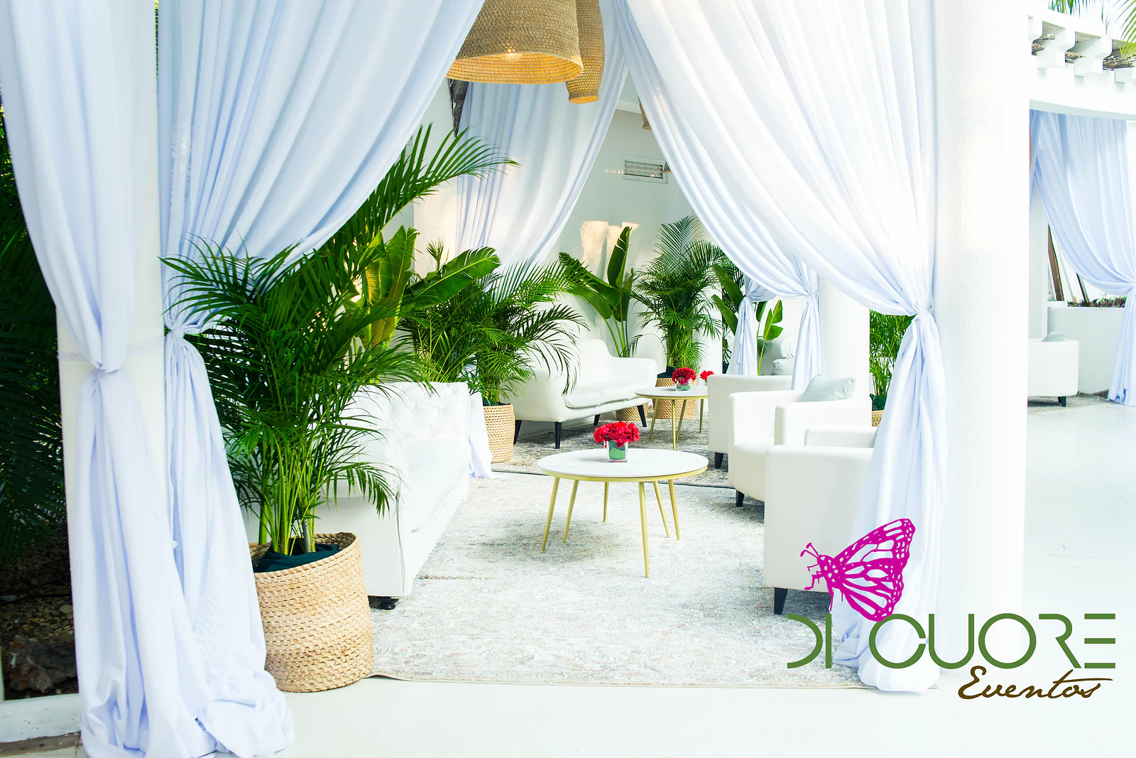 Lounge corner entirely in white, with sofas and armchairs, a coffee table on gold legs, palms in straw baskets and white drapes