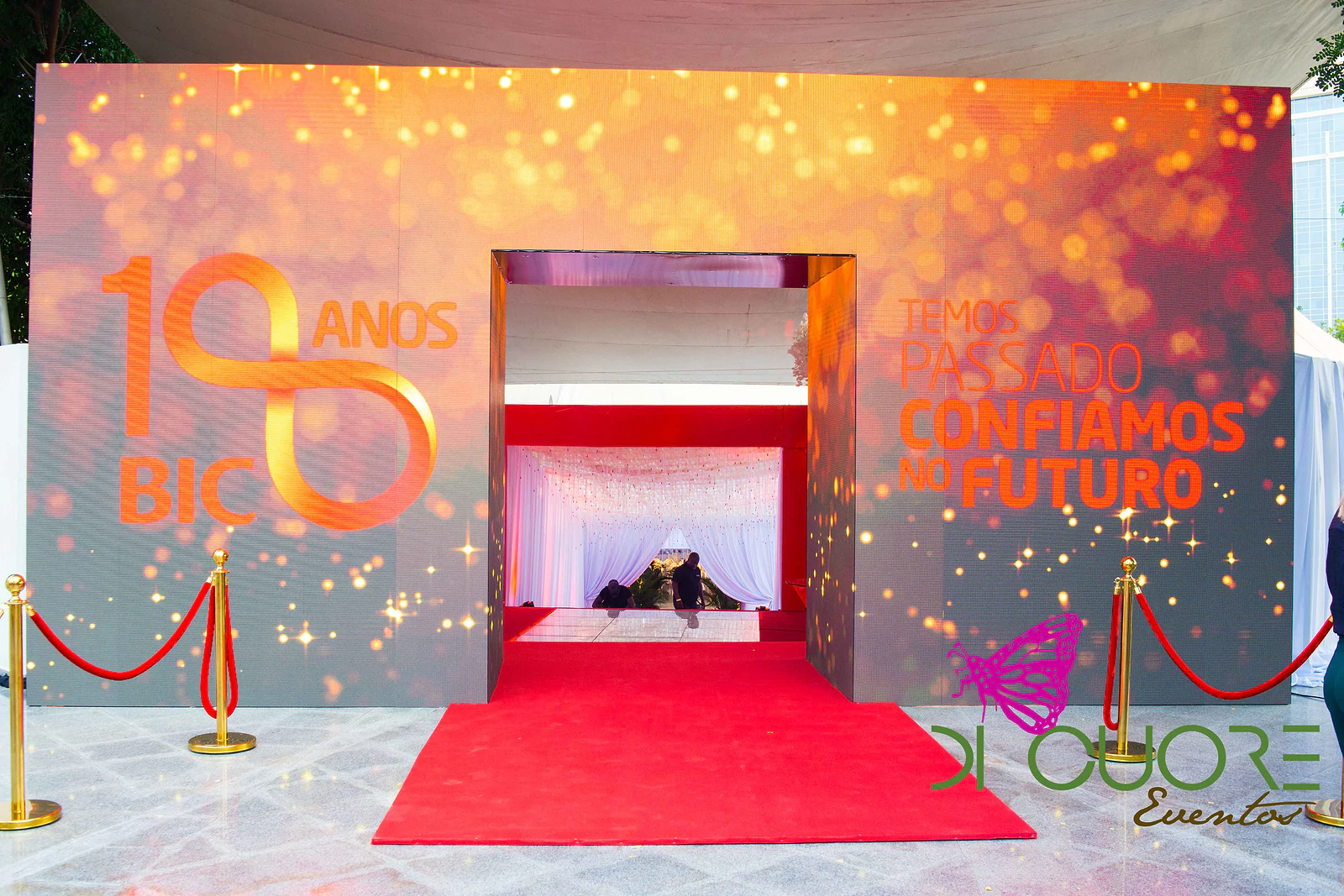 Illuminated panel with the 18 anos BIC logo and the motto “Confiamos no futuro”, with a red carpet, velvet ropes and gold posts