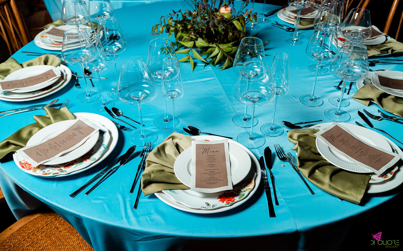 Round table with a turquoise cloth, plates, olive-green napkins and kraft-paper menus