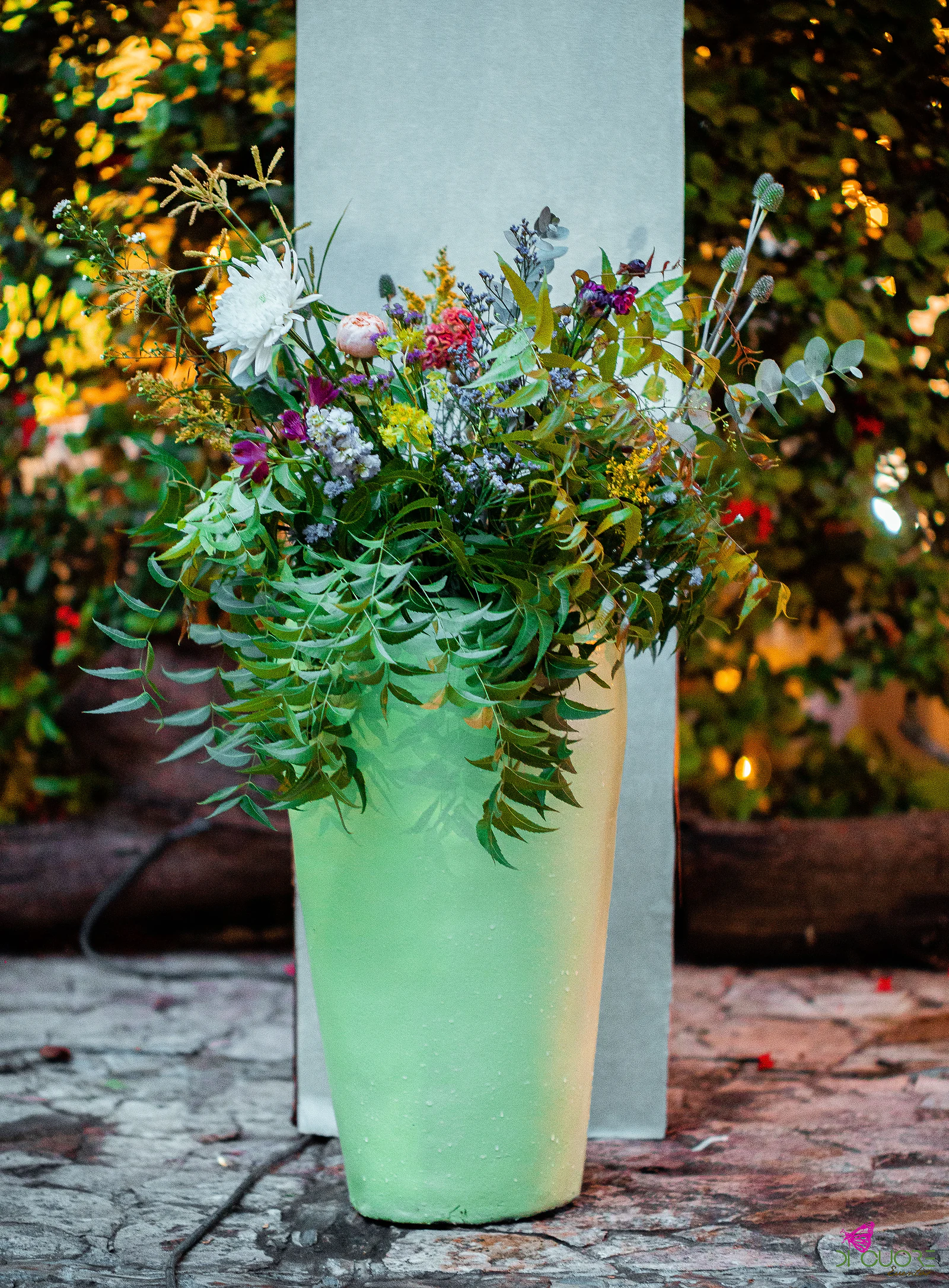 Tall mint-green vase of wildflowers and foliage beside a white column