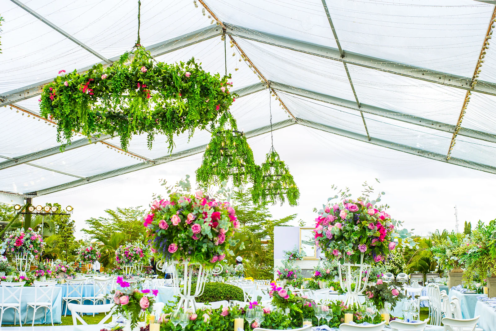 A ring of hanging foliage above the tables, with tall pink rose arrangements on white stands behind.