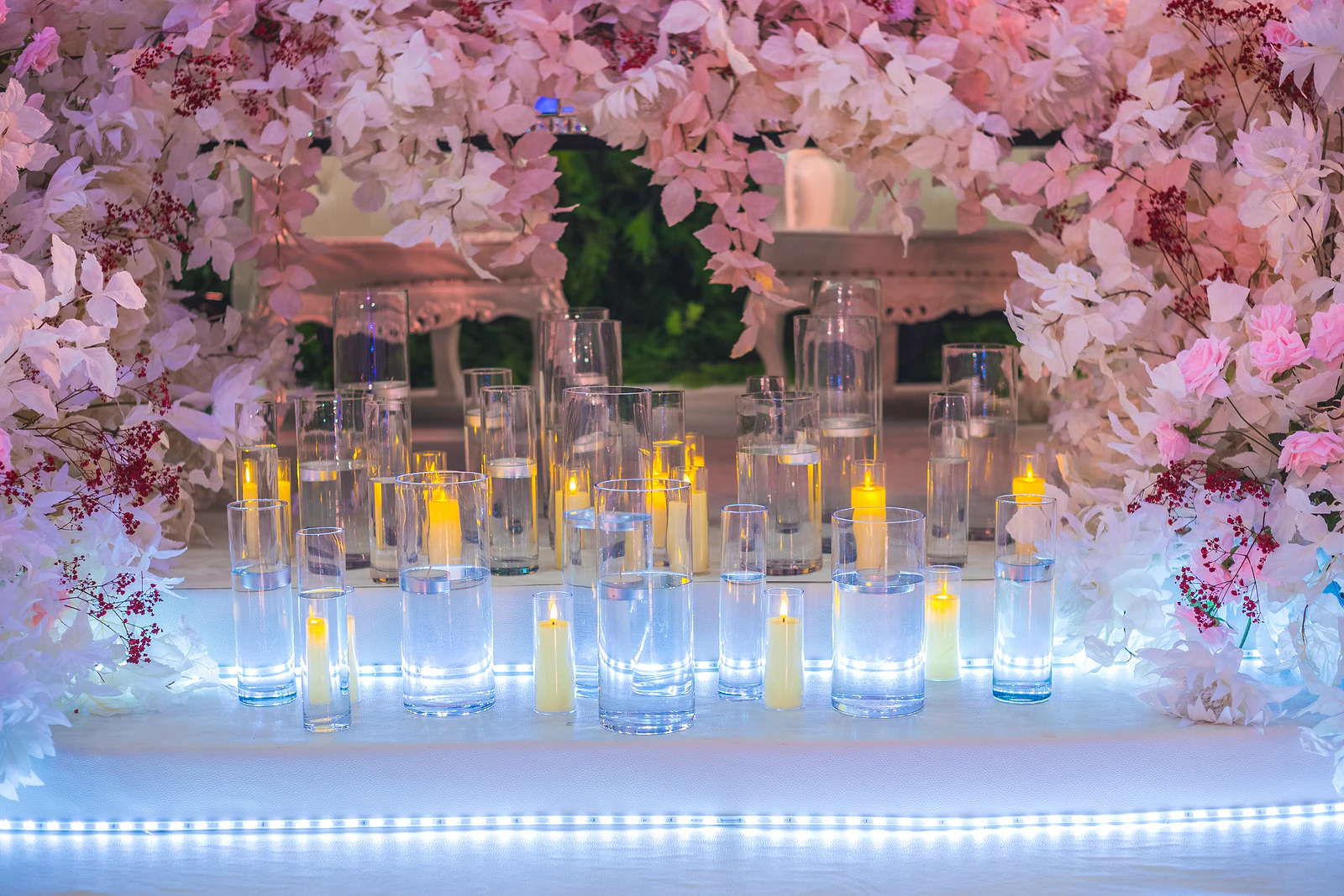 Velas em cilindros de vidro sobre o degrau iluminado a LED, sob ramos de flores cor-de-rosa e brancas