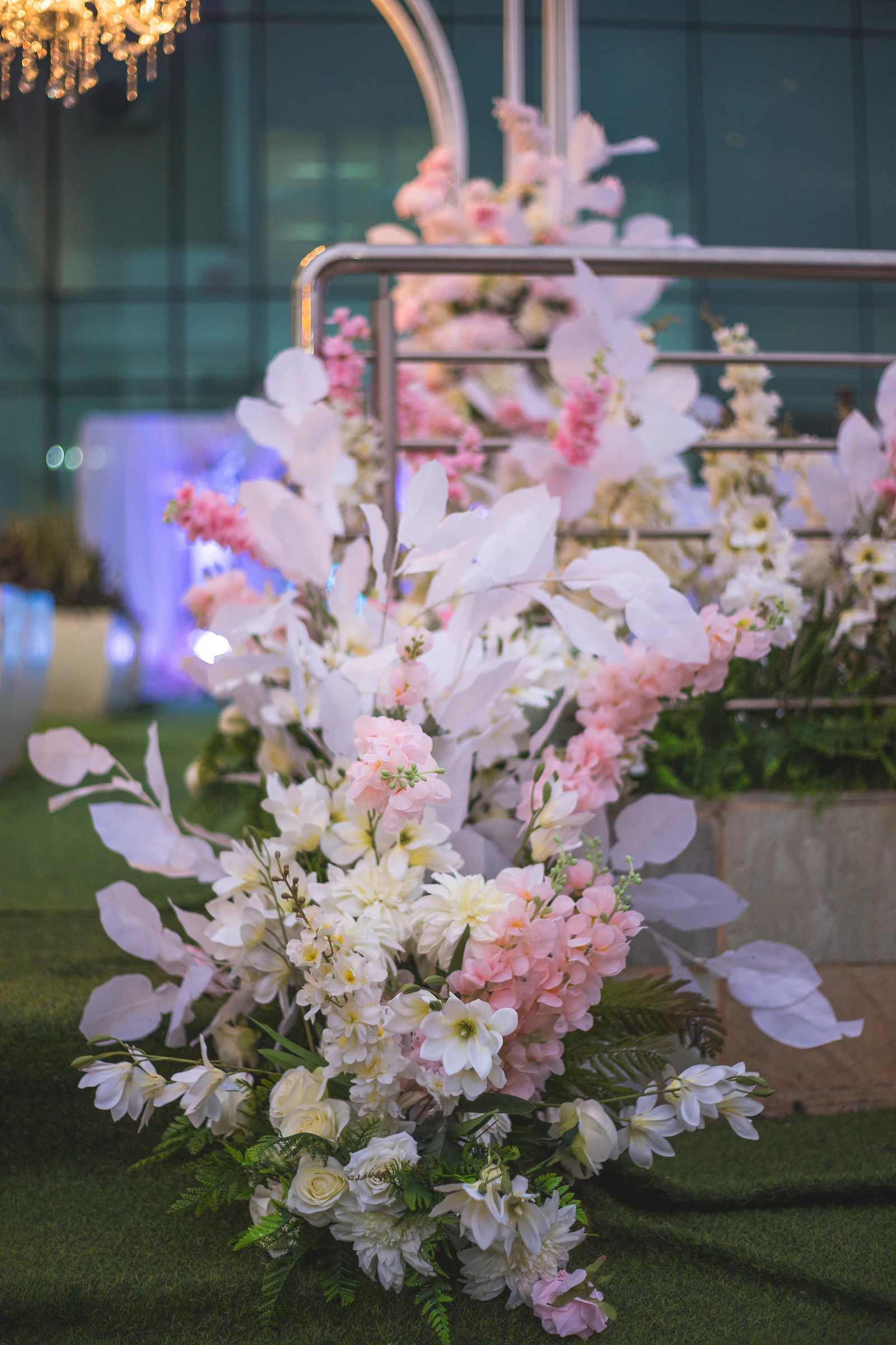 Ramo de flores brancas e cor-de-rosa com folhas claras e fetos, sobre a relva junto a uma estrutura de metal