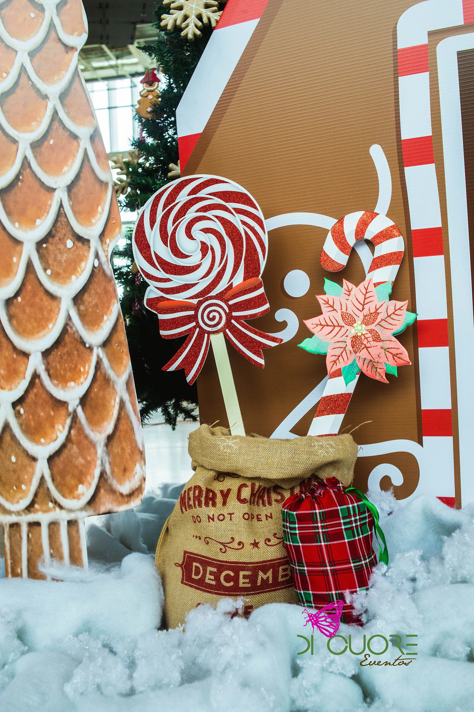 Pirulito vermelho e branco com laço, bengala de açúcar com flor de Natal, saco de serapilheira e prenda axadrezada sobre neve de algodão
