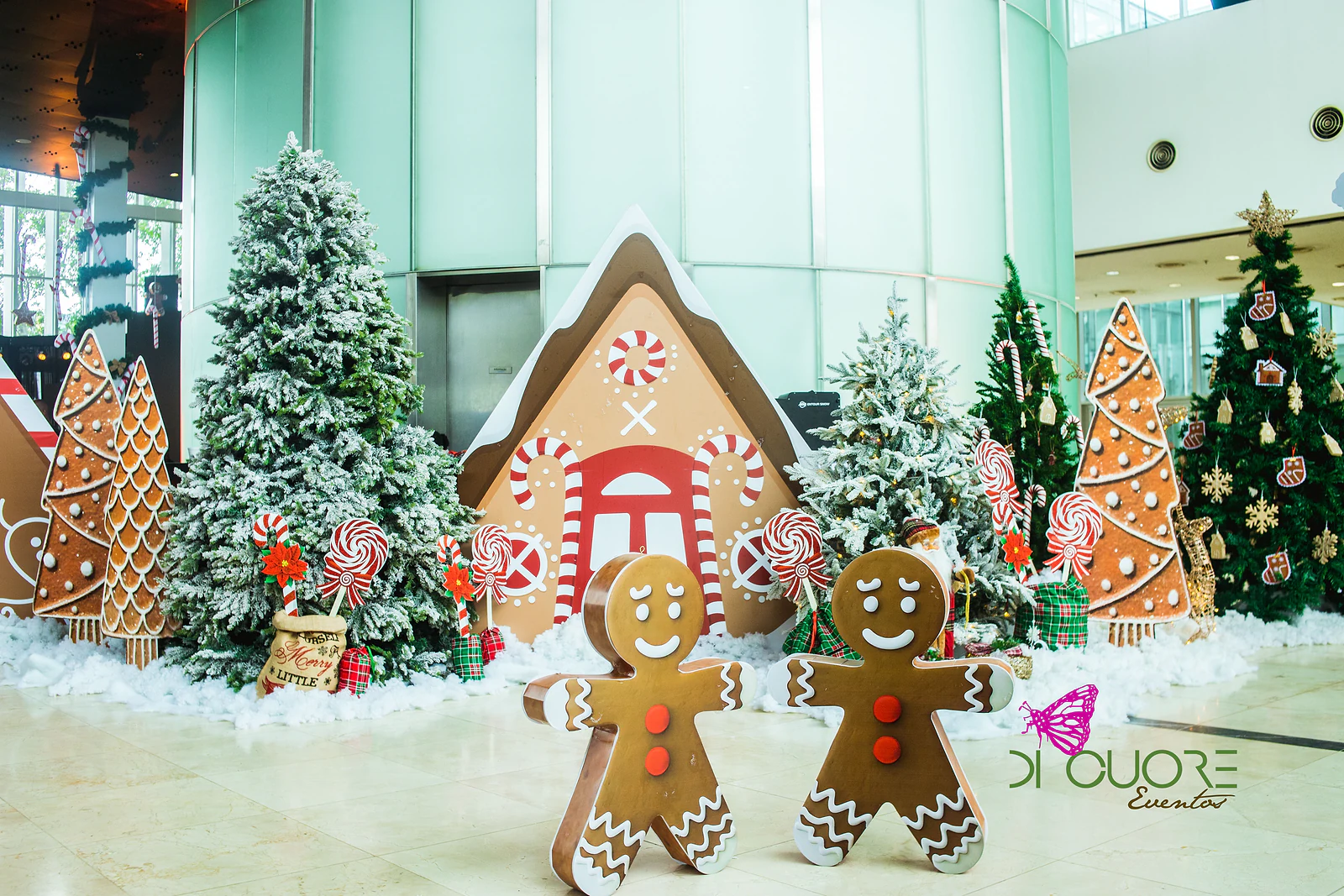 Duas figuras de gengibre à frente de uma casinha de bolacha, árvores nevadas, pirulitos e neve de algodão