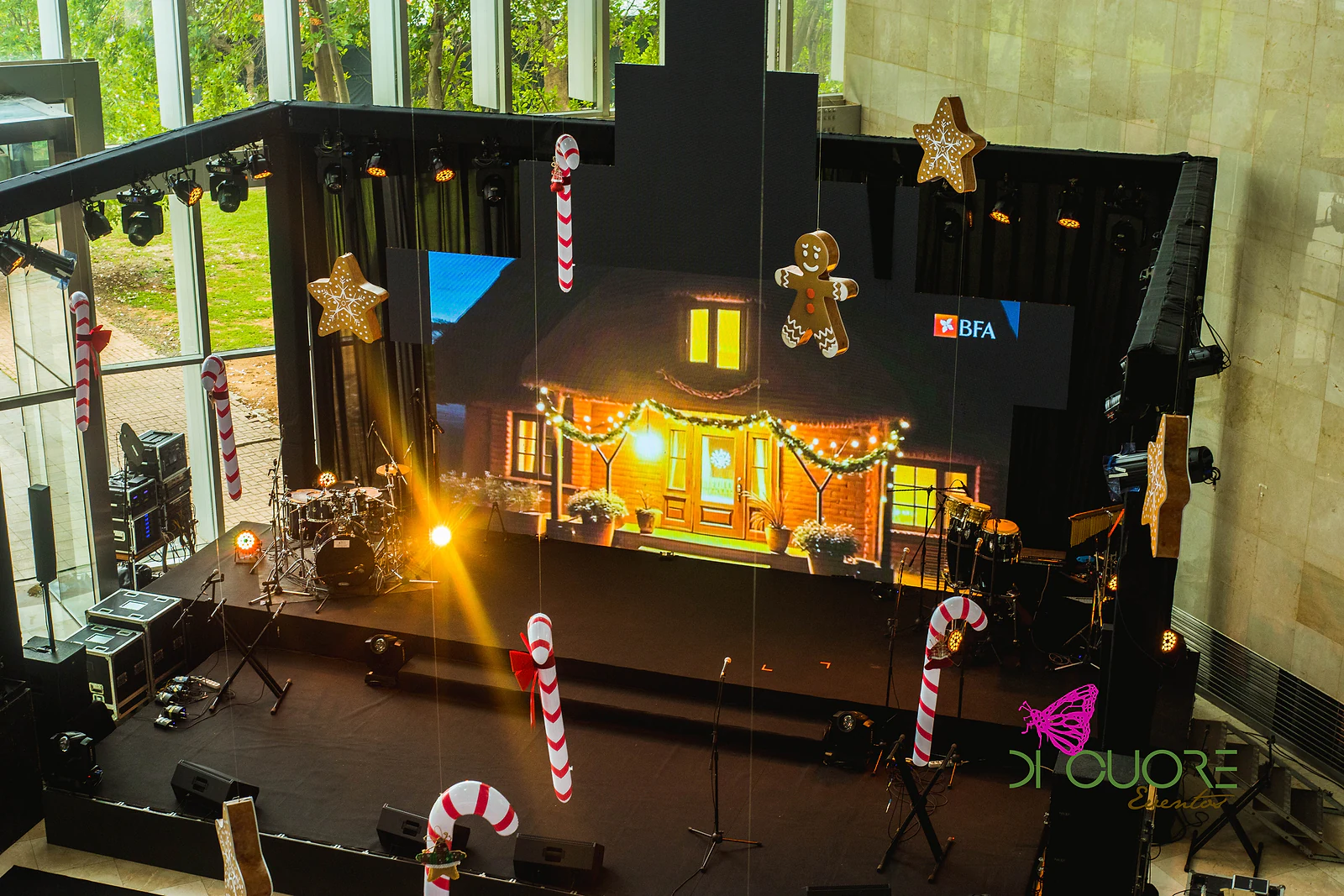 Palco com ecrã, bateria e instrumentos, rodeado de bengalas de açúcar, estrelas e bonecos de gengibre suspensos
