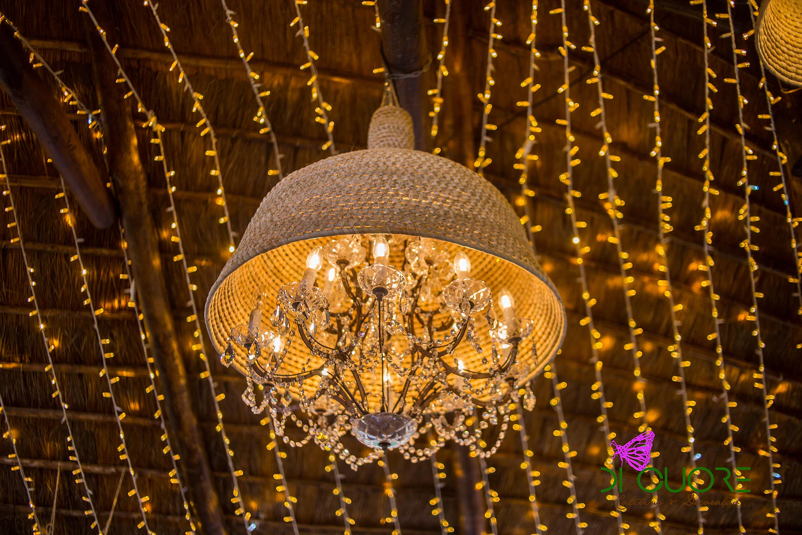 Lustre de cristal dentro de uma cúpula de vime, suspenso de um tecto de palha coberto de fios de luzes