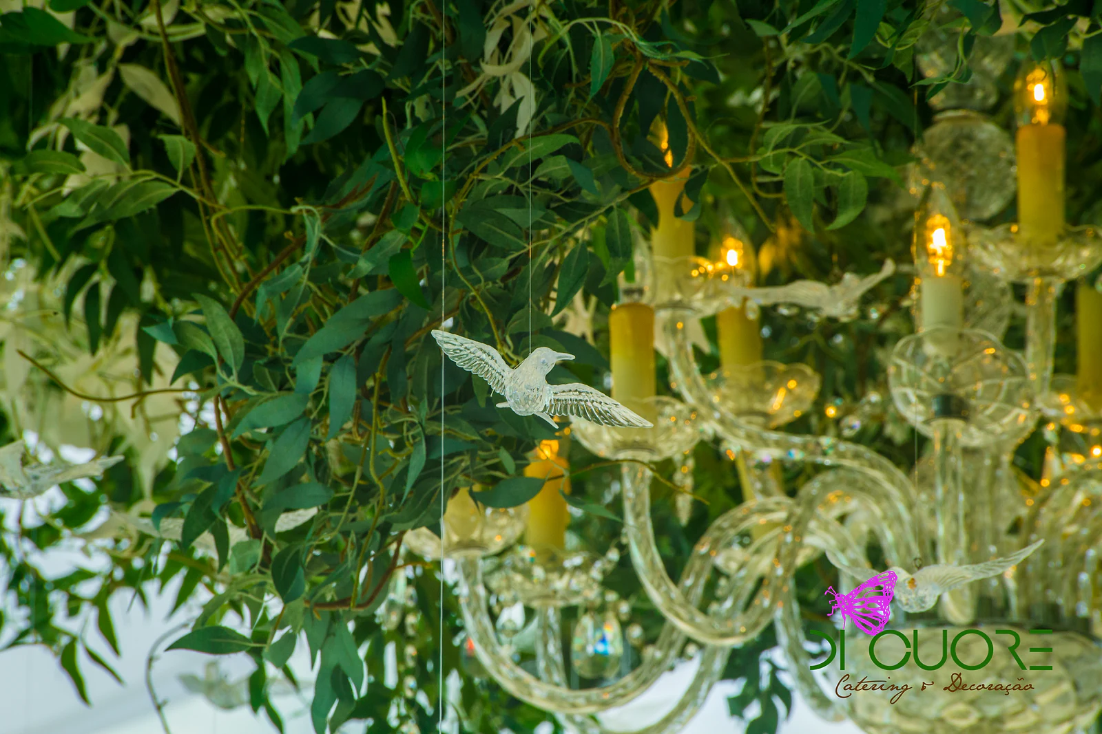 Lustre de cristal com velas entre ramos de folhagem, com pequenas pombas de vidro suspensas