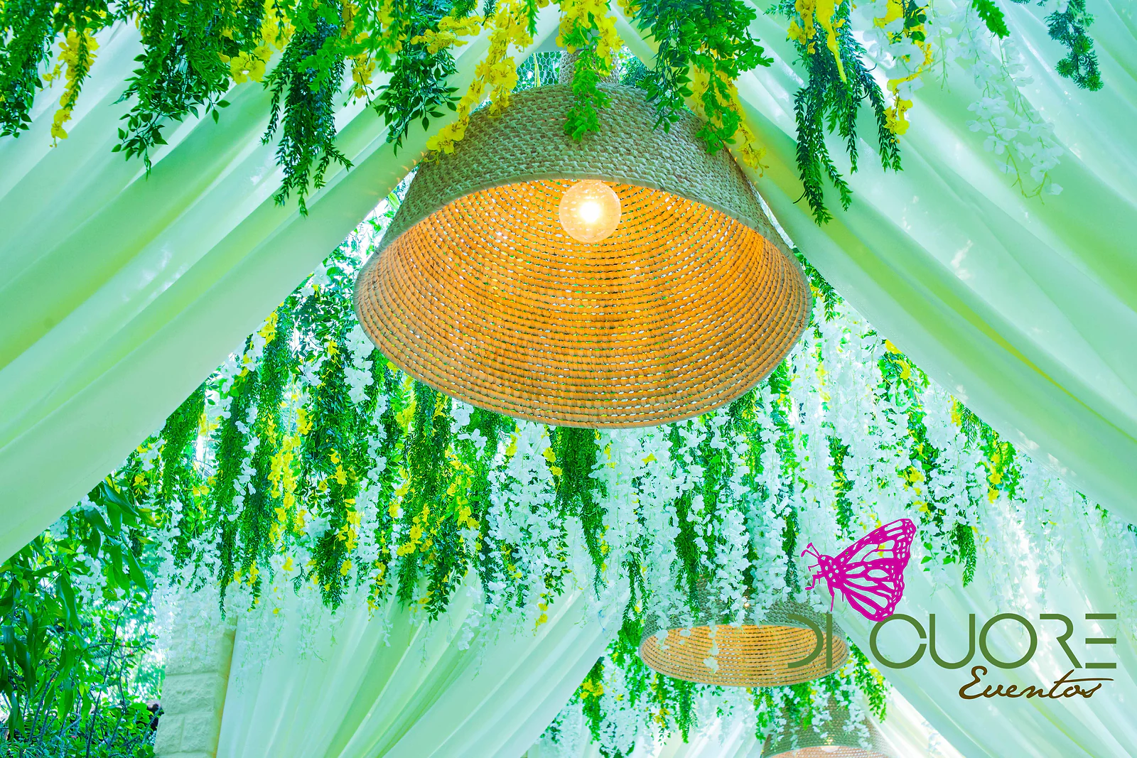 Lit woven straw lamp hanging between pale drapes and a cascade of white flowers and foliage