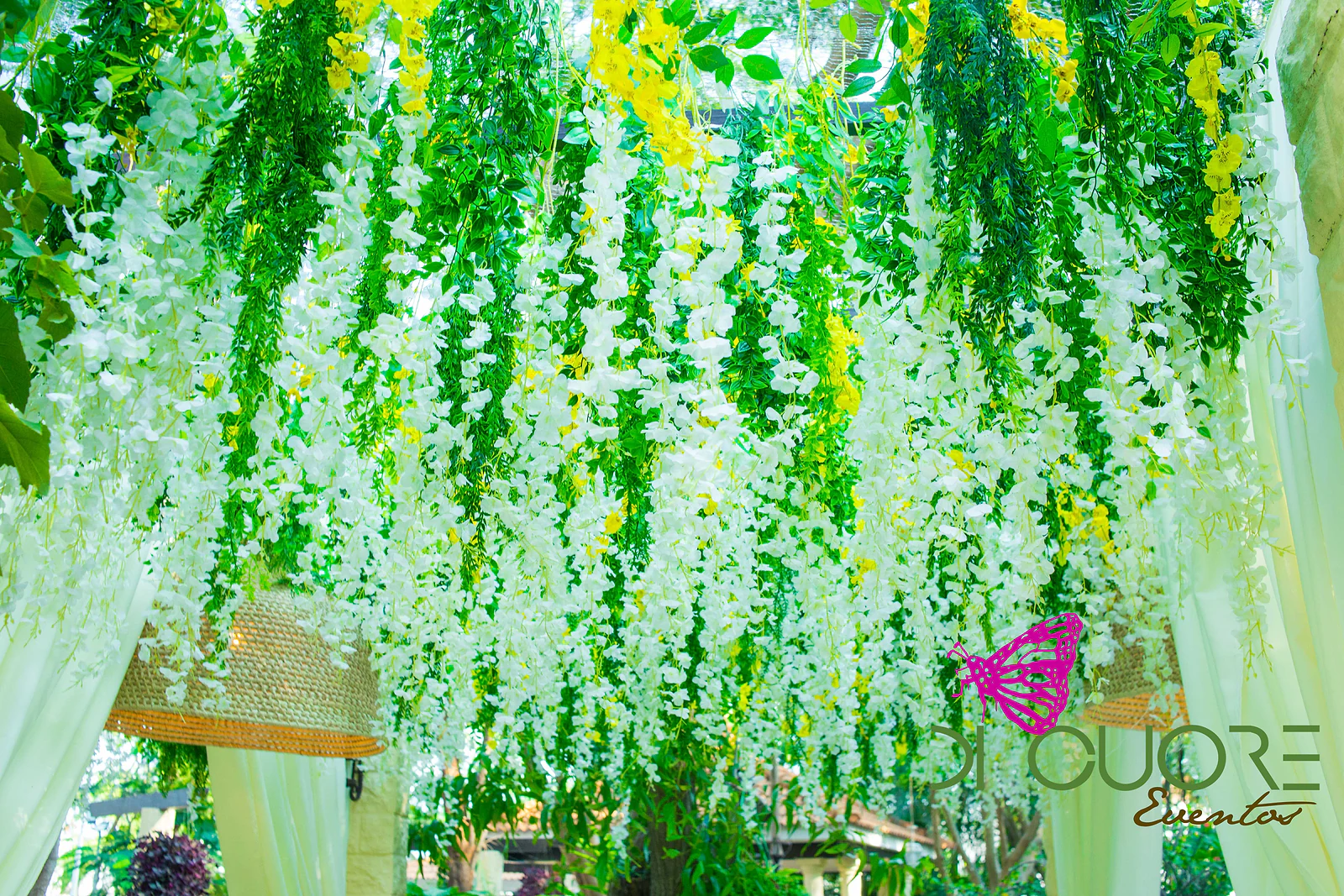 Ceiling of hanging white flowers and foliage, with woven straw lamps and pale drapes at the sides