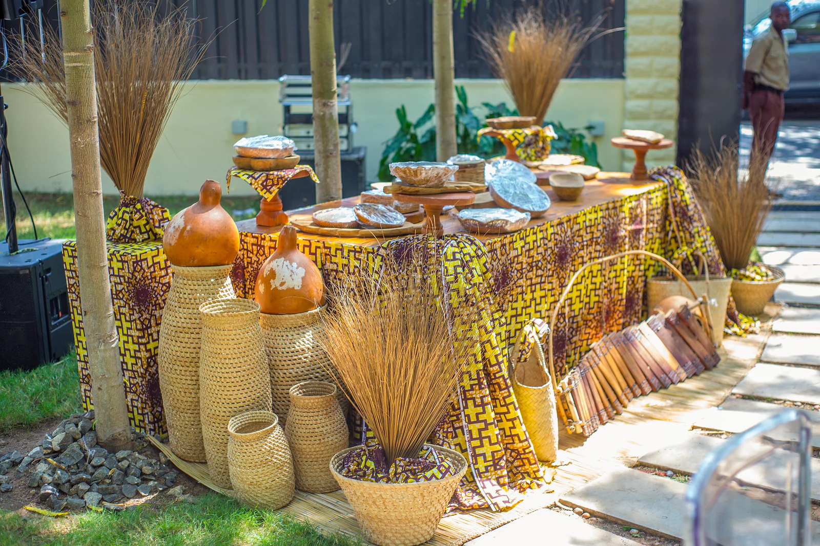 Buffet table covered in yellow and purple printed fabric, with straw baskets, gourds and bunches of dried grass
