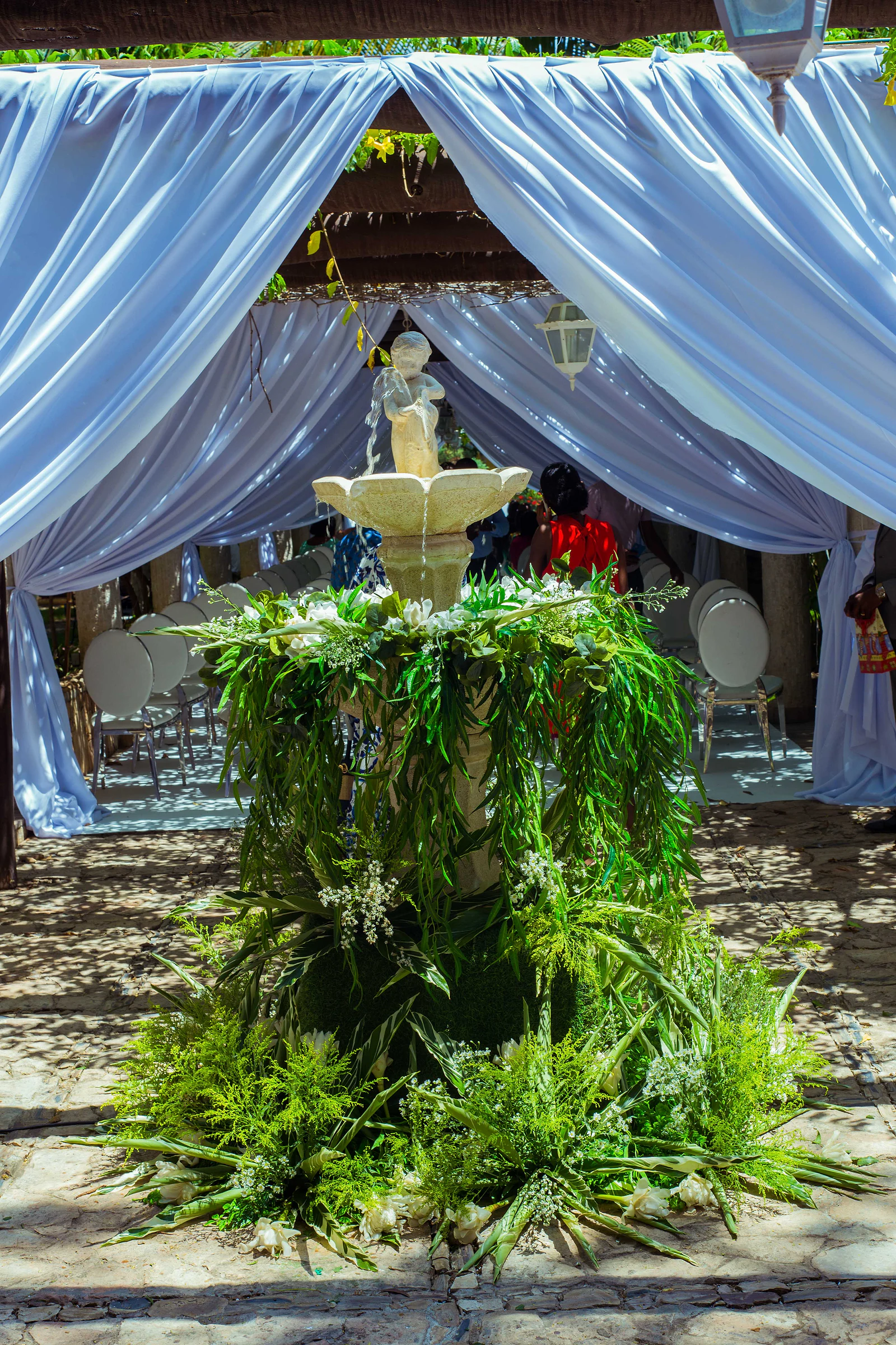 A stone fountain with a statue, ringed with foliage and gypsophila, in front of a pavilion of pale blue drapes