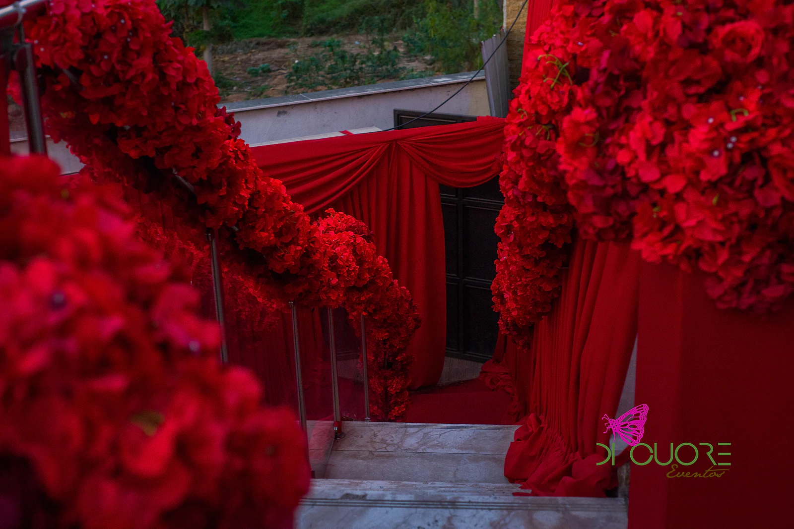 Guirlandas de rosas vermelhas ao longo do corrimão da escadaria, entre cortinados rubros