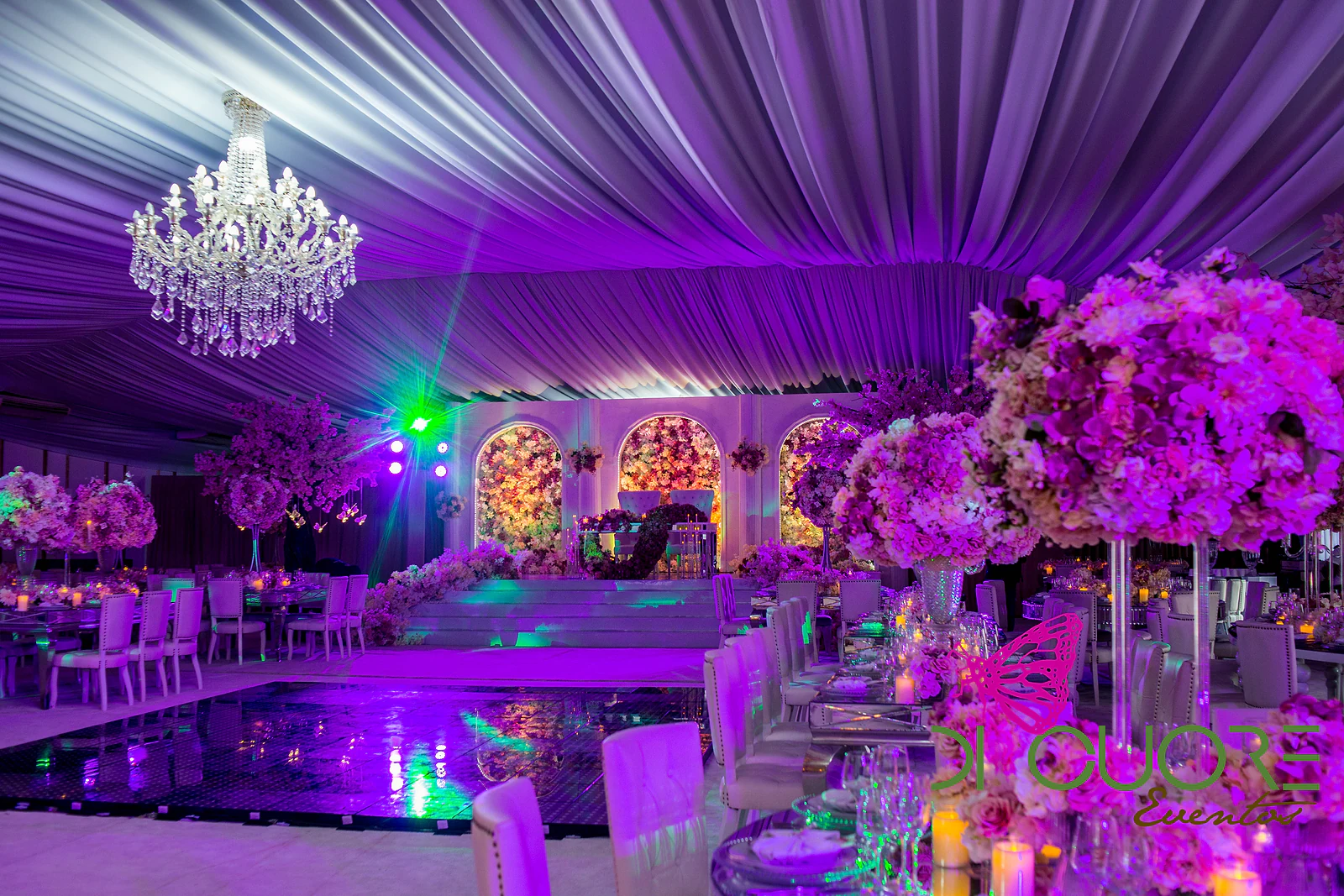 Hall beneath a lilac draped ceiling, with a crystal chandelier, mirrored tables, tall centrepieces and the flower stage at the far end.