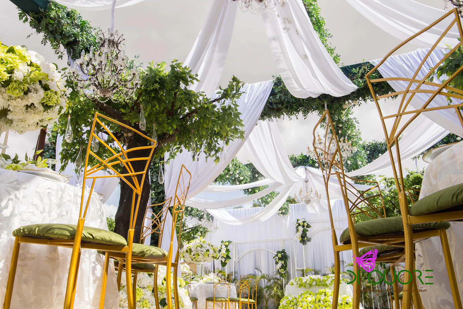 Gold chairs with green seats beneath a tree hung with glass droplets and white drapes