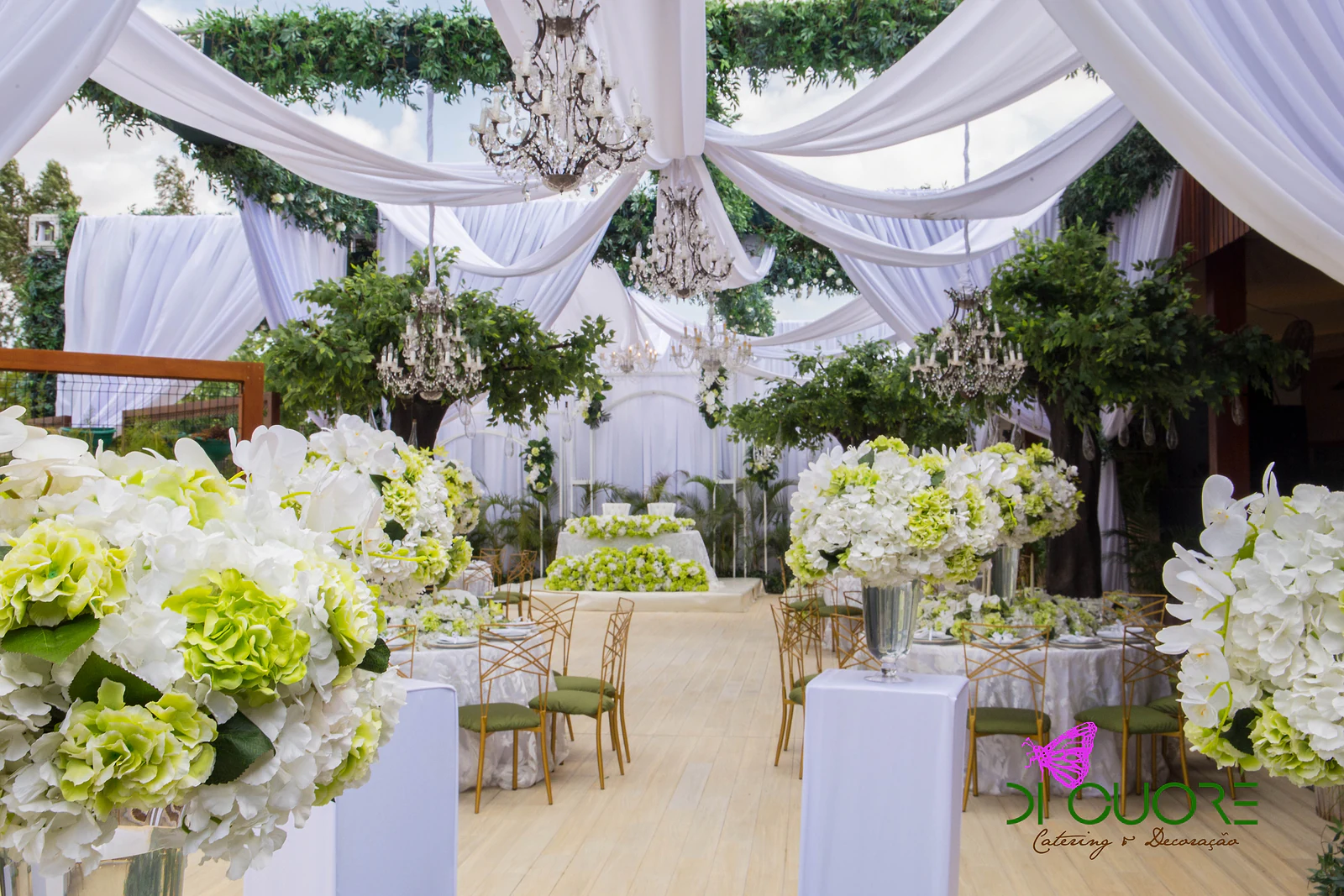 Walkway between the tables, with hydrangea and orchid arrangements in the foreground and chandeliers and white drapes overhead