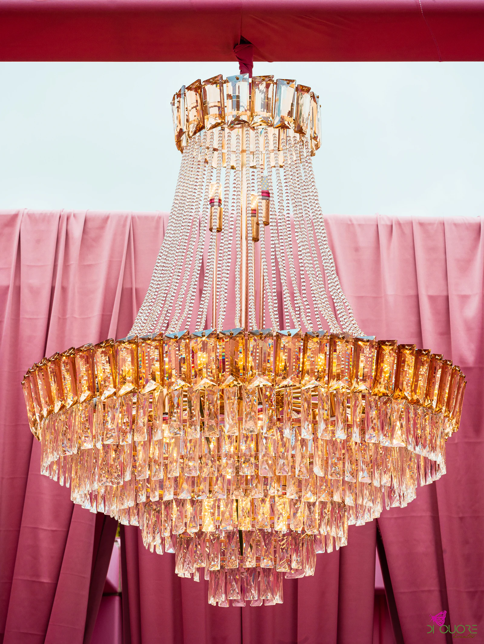 Lustre de cristal com pendentes dourados diante de cortinados cor-de-rosa