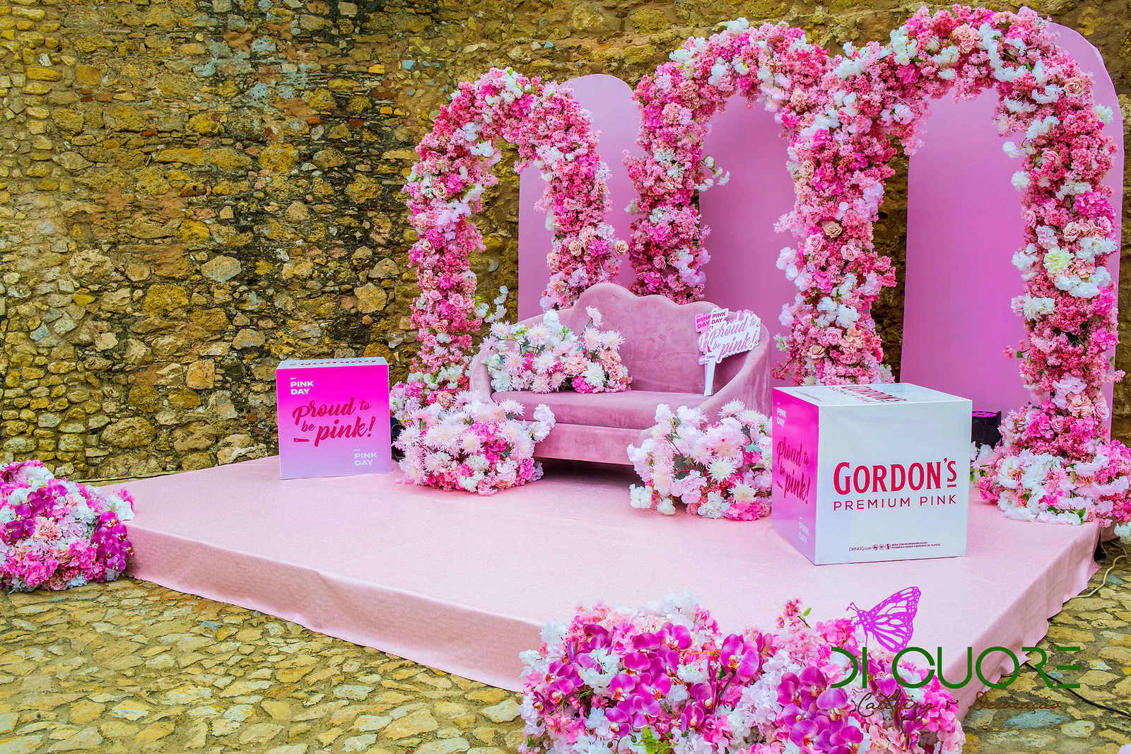 Estrado rosa com três arcos de flores em frente à muralha de pedra, com um sofá rosa entre cubos Gordon’s Premium Pink