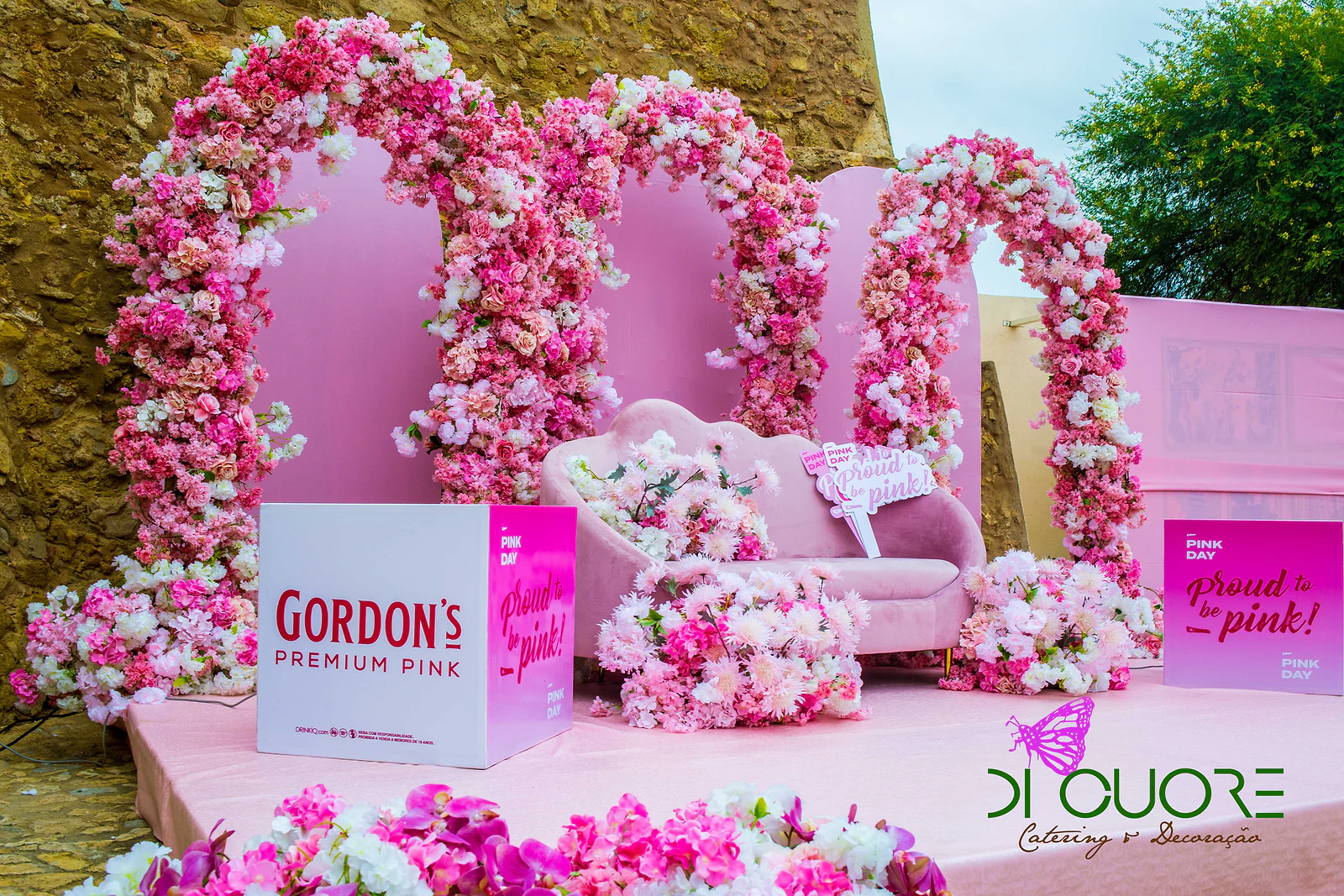 Arcos de flores cor-de-rosa sobre o estrado rosa, com sofá, cubo Gordon’s Premium Pink e maciços de flores fúcsia à frente
