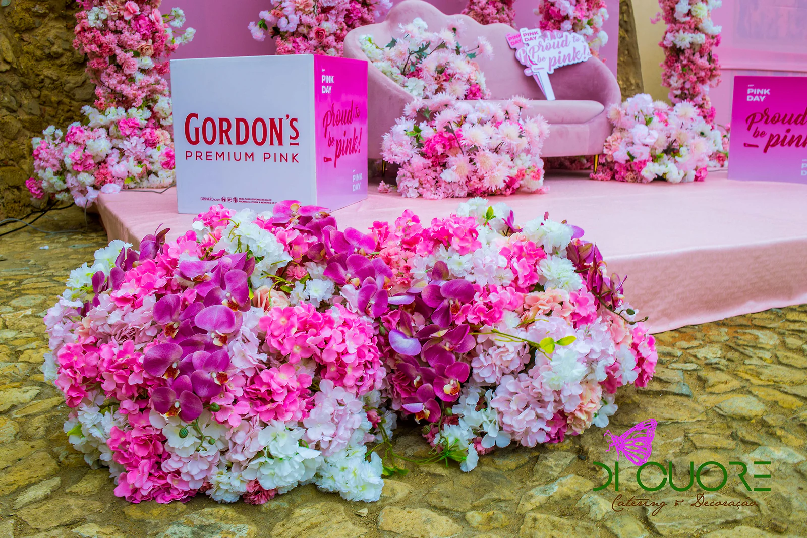 Maciço de flores fúcsia, roxas e brancas junto ao estrado, com um cubo Gordon’s Premium Pink ao fundo