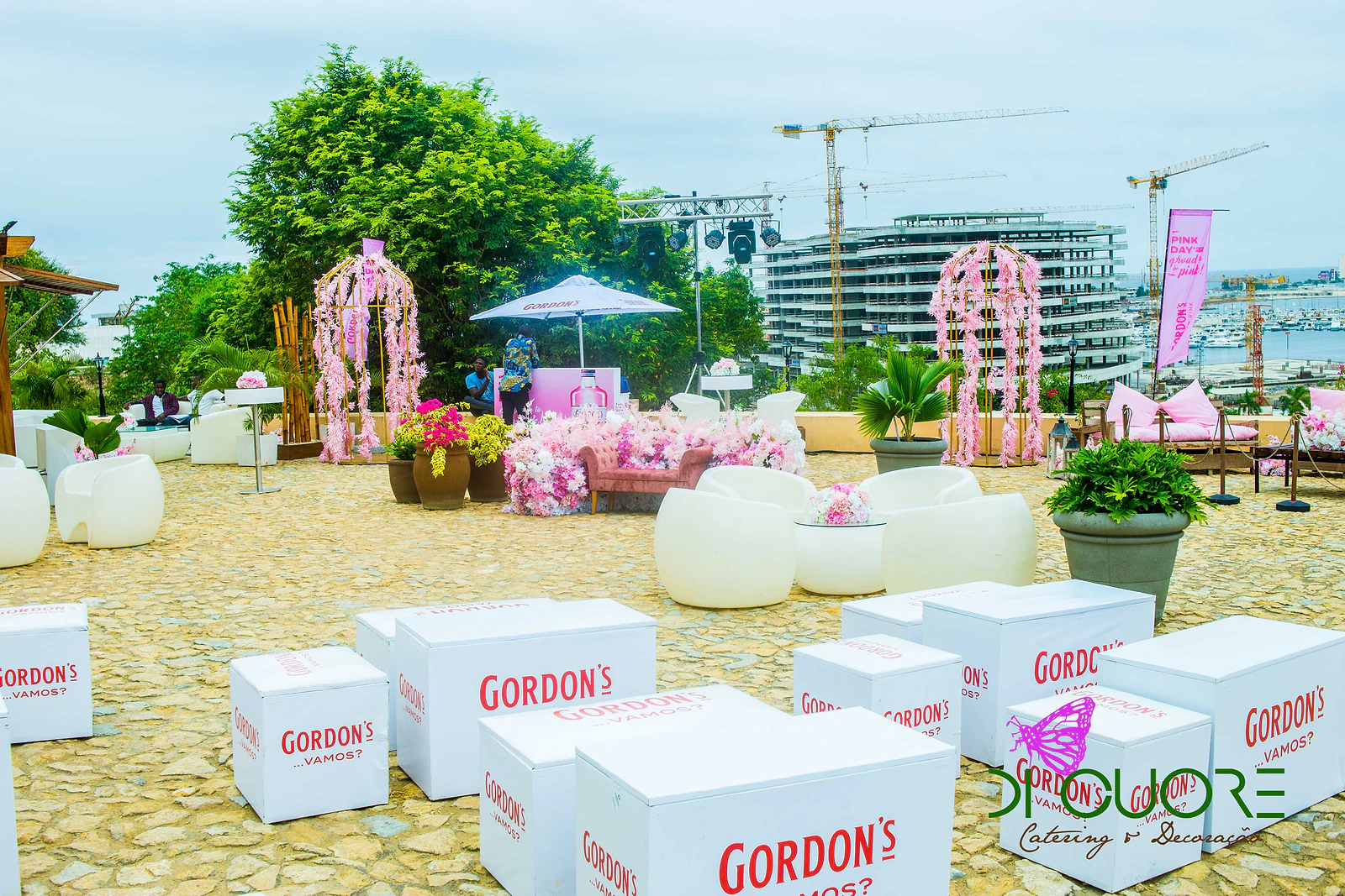 Cubos brancos Gordon’s e poltronas brancas no pátio de calçada, com pavilhões de flores cor-de-rosa e a cidade ao fundo