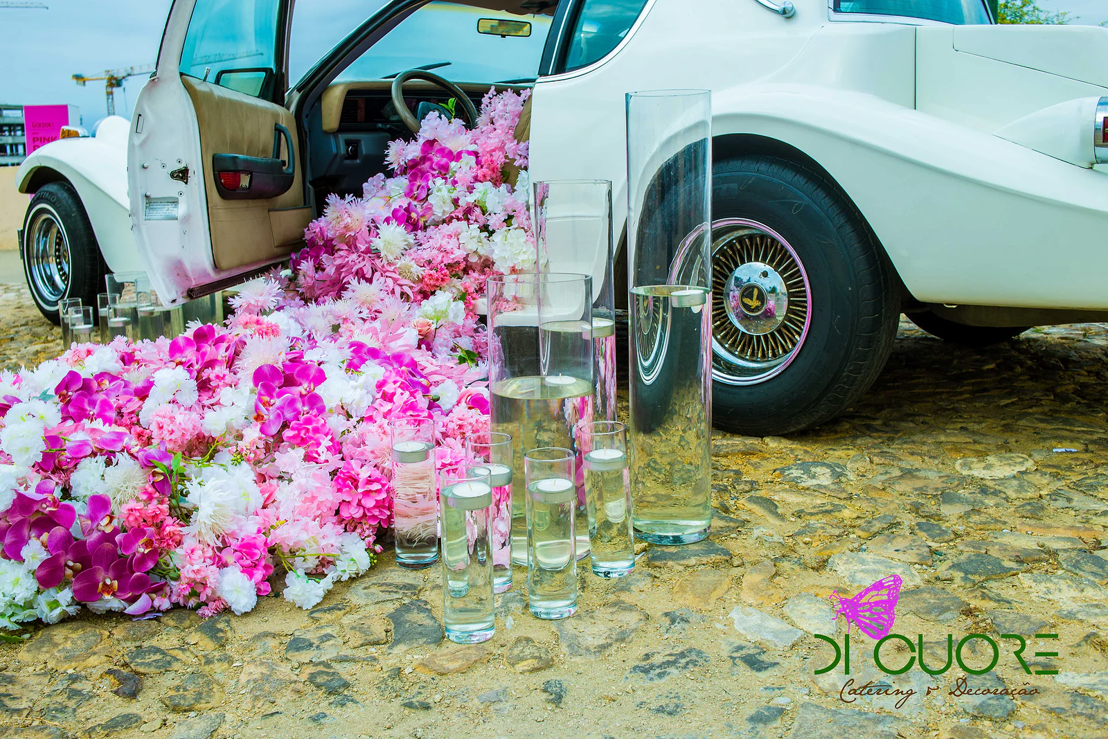 Cascata de orquídeas e flores fúcsia, rosa e brancas a escorrer do carro, entre jarras altas de vidro com água