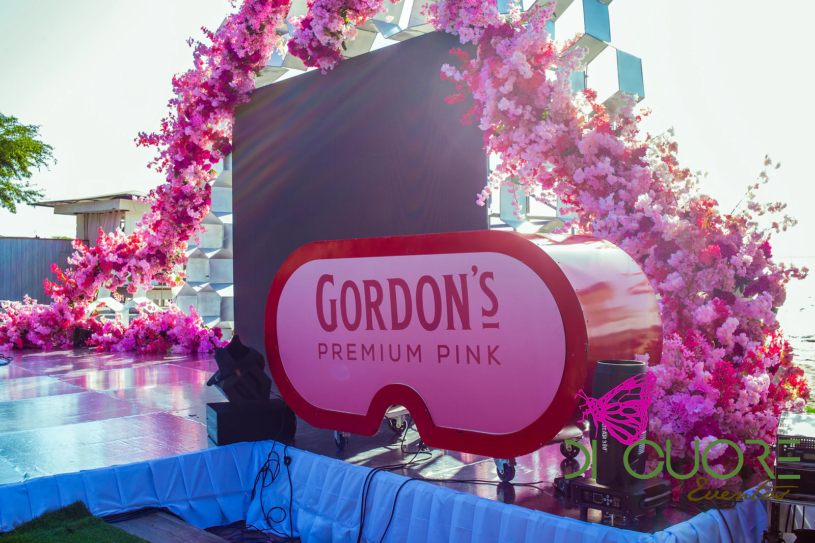 Arco de flores cor-de-rosa e fúcsia sobre uma estrutura de favos brancos, com um letreiro Gordon’s Premium Pink em primeiro plano