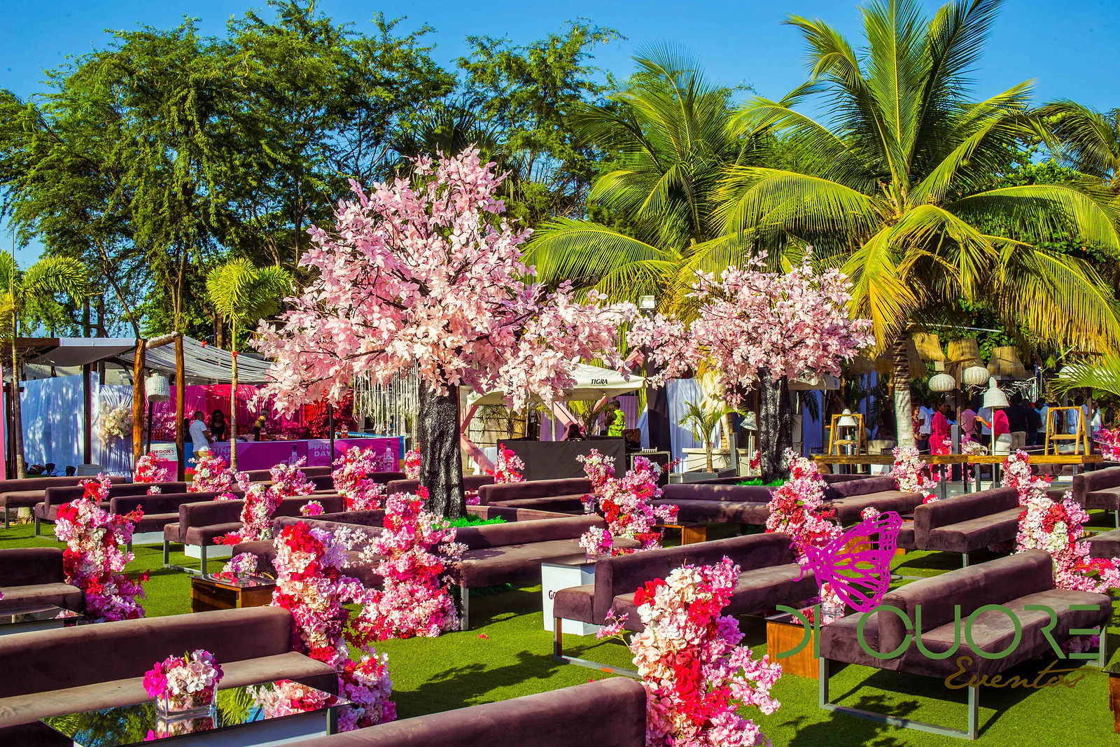 Bancos de veludo castanho entre cerejeiras de flores cor-de-rosa e palmeiras, com arranjos altos de flores fúcsia e vermelhas