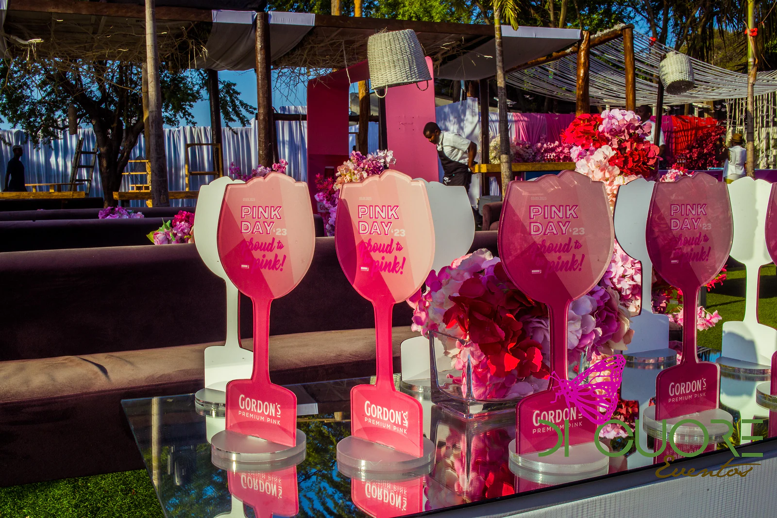 Letreiros cor-de-rosa em forma de taça, com a frase Pink Day, sobre uma mesa espelhada com flores cor-de-rosa e vermelhas