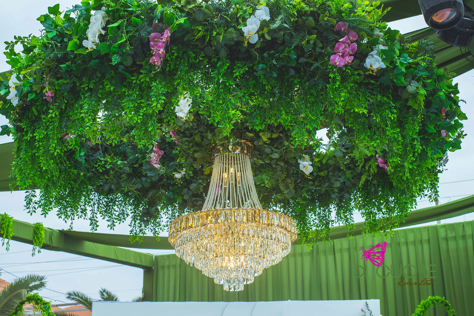 Aro suspenso de folhagem com orquídeas rosa e brancas e um lustre dourado de cristal ao centro