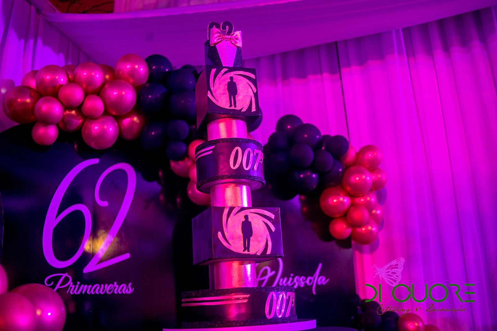 Pormenor do painel com o número 62 e a palavra “Primaveras” e do bolo de andares com o símbolo 007, entre balões magenta e pretos
