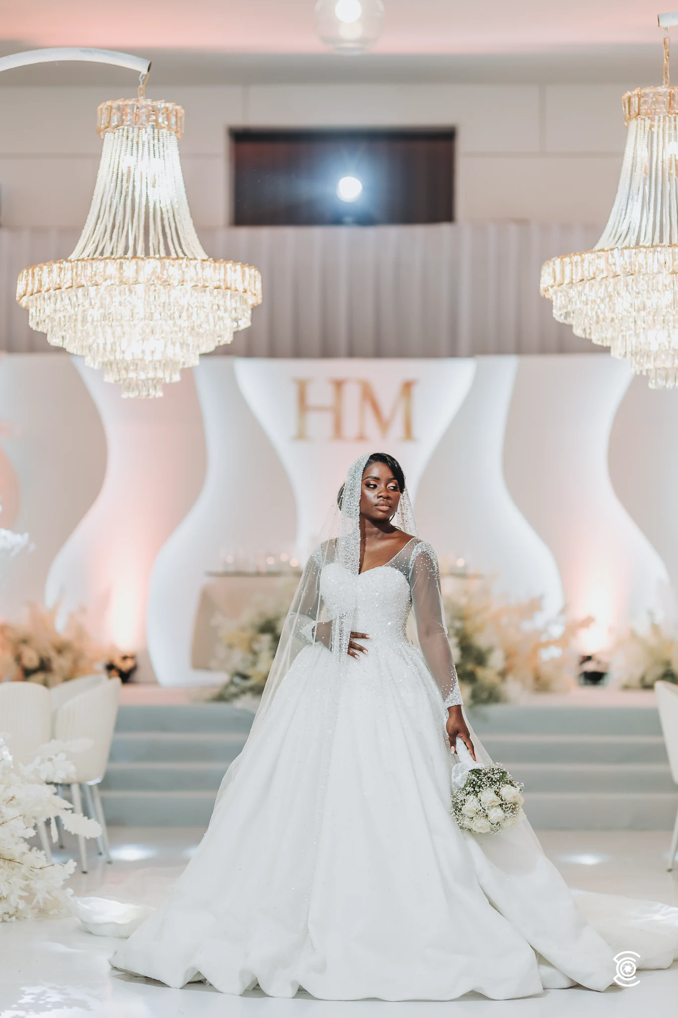 The bride in front of the stage with the HM monogram and chandeliers