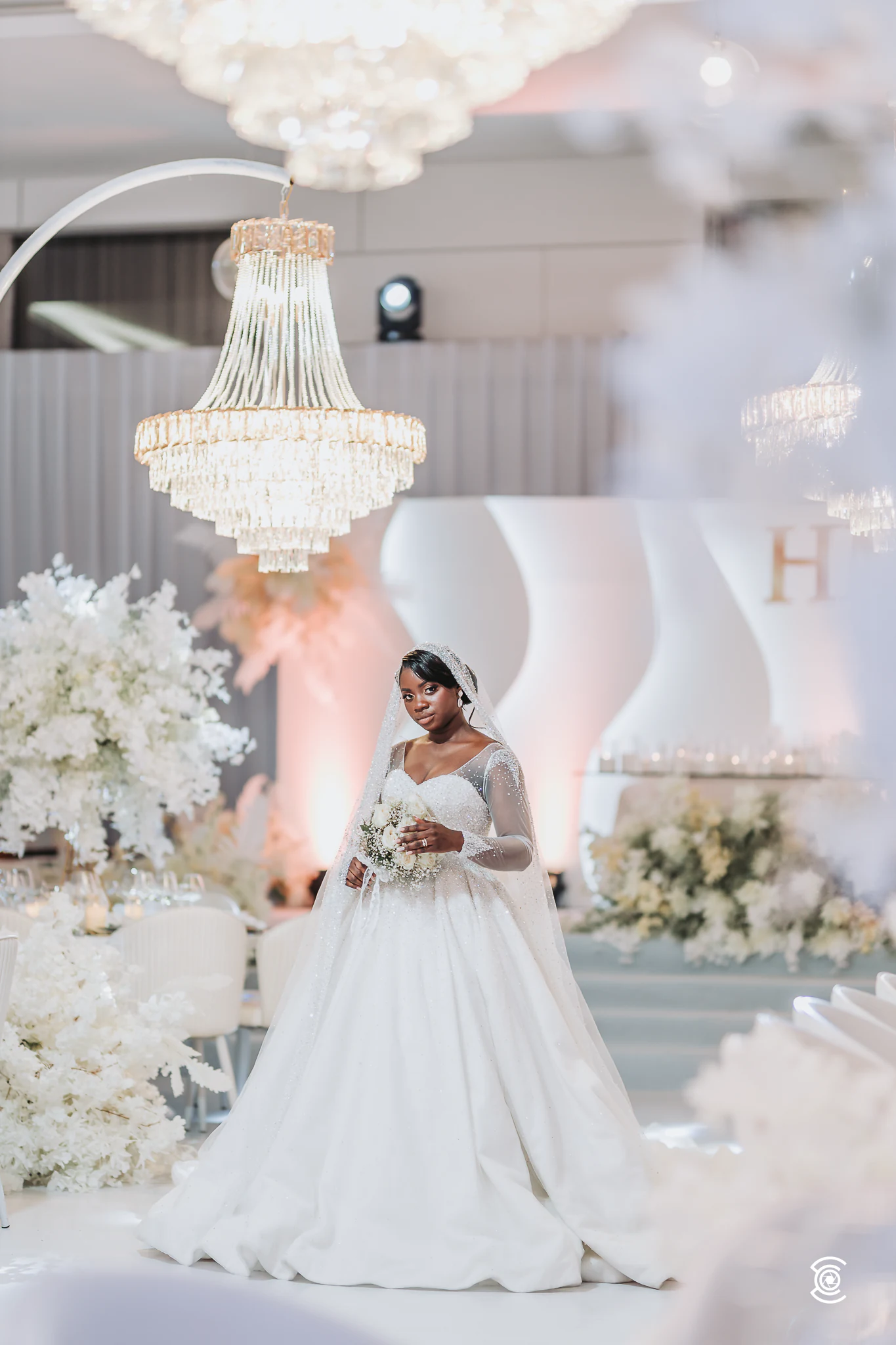 A noiva de bouquet na mão, entre lustres e flores brancas