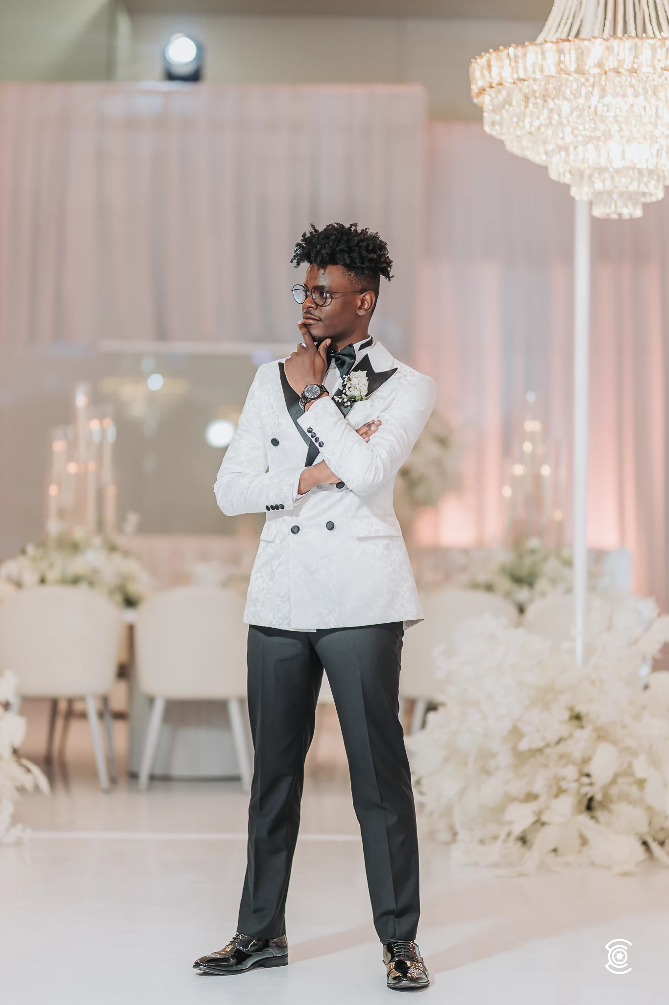 O noivo de smoking branco posa no salão iluminado